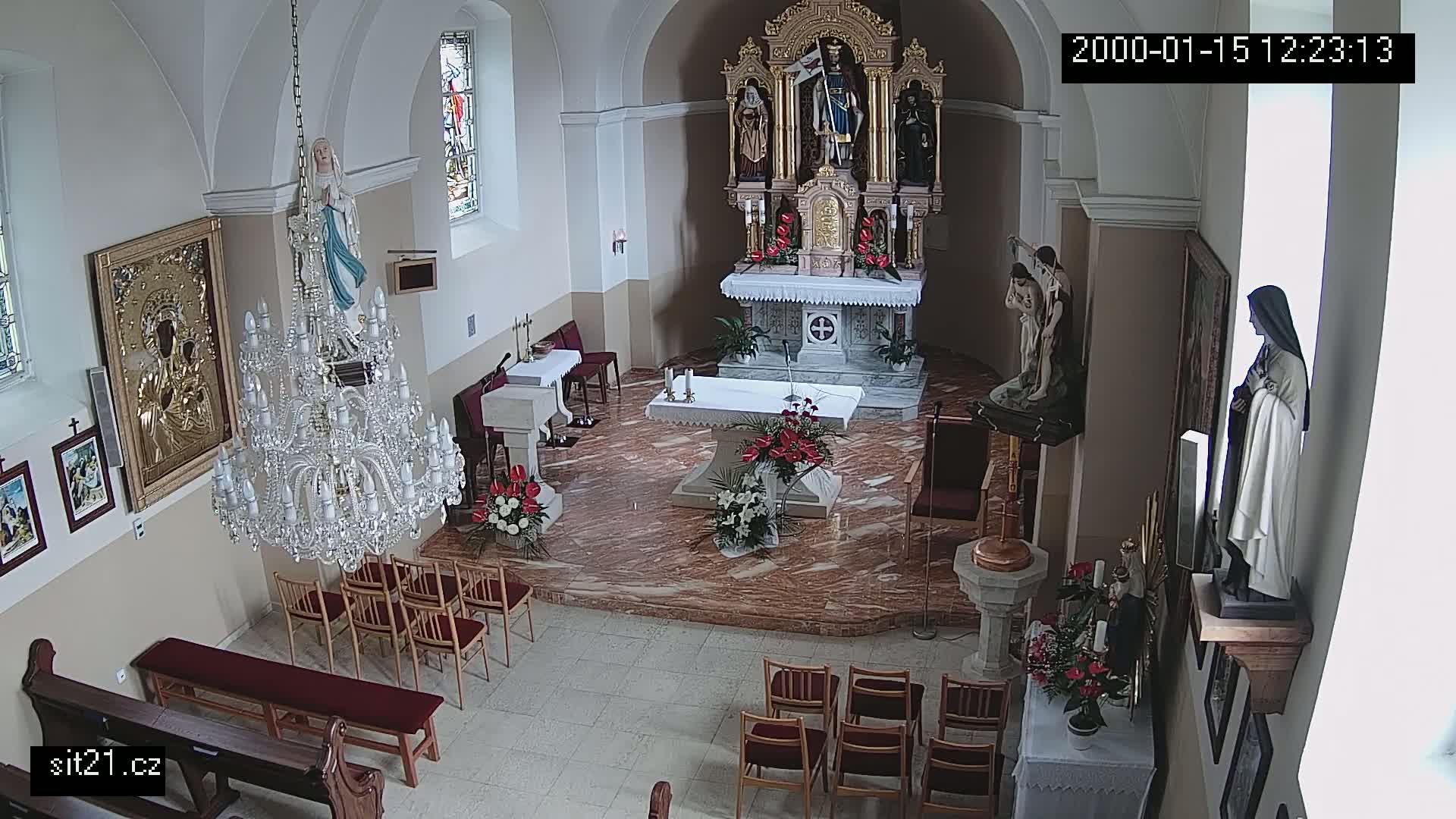 An indoor view of a church sanctuary, featuring a marble altar, several religious statues, a large crystal chandelier, and rows of empty chairs.