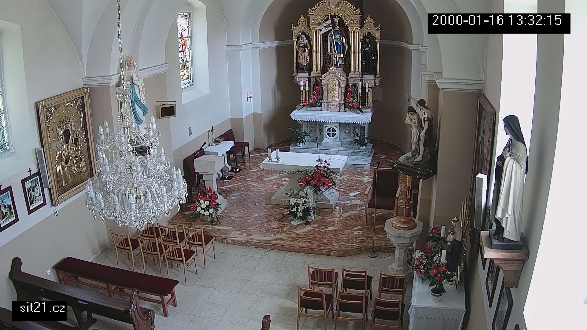 An indoor church sanctuary with a marble floor, ornate altar, several religious statues, a large crystal chandelier, and rows of empty chairs.
