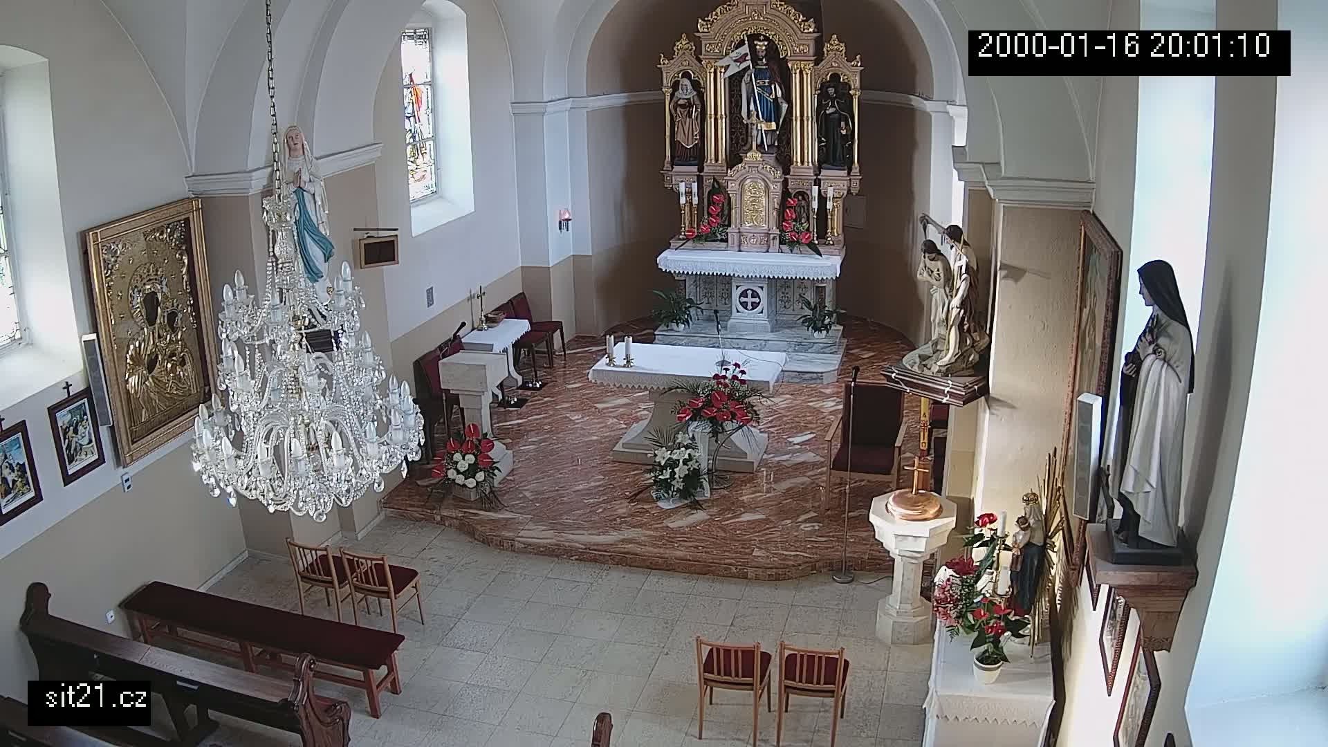 An indoor view of a church's altar area, showing statues, candles, and a large crystal chandelier.