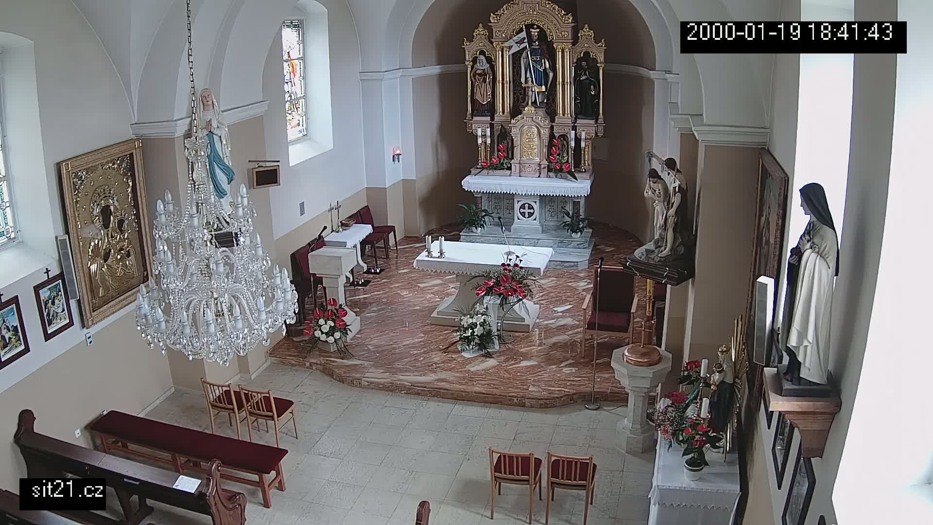An indoor view of a church sanctuary, featuring an altar, statues, a chandelier, and several religious paintings on the walls.