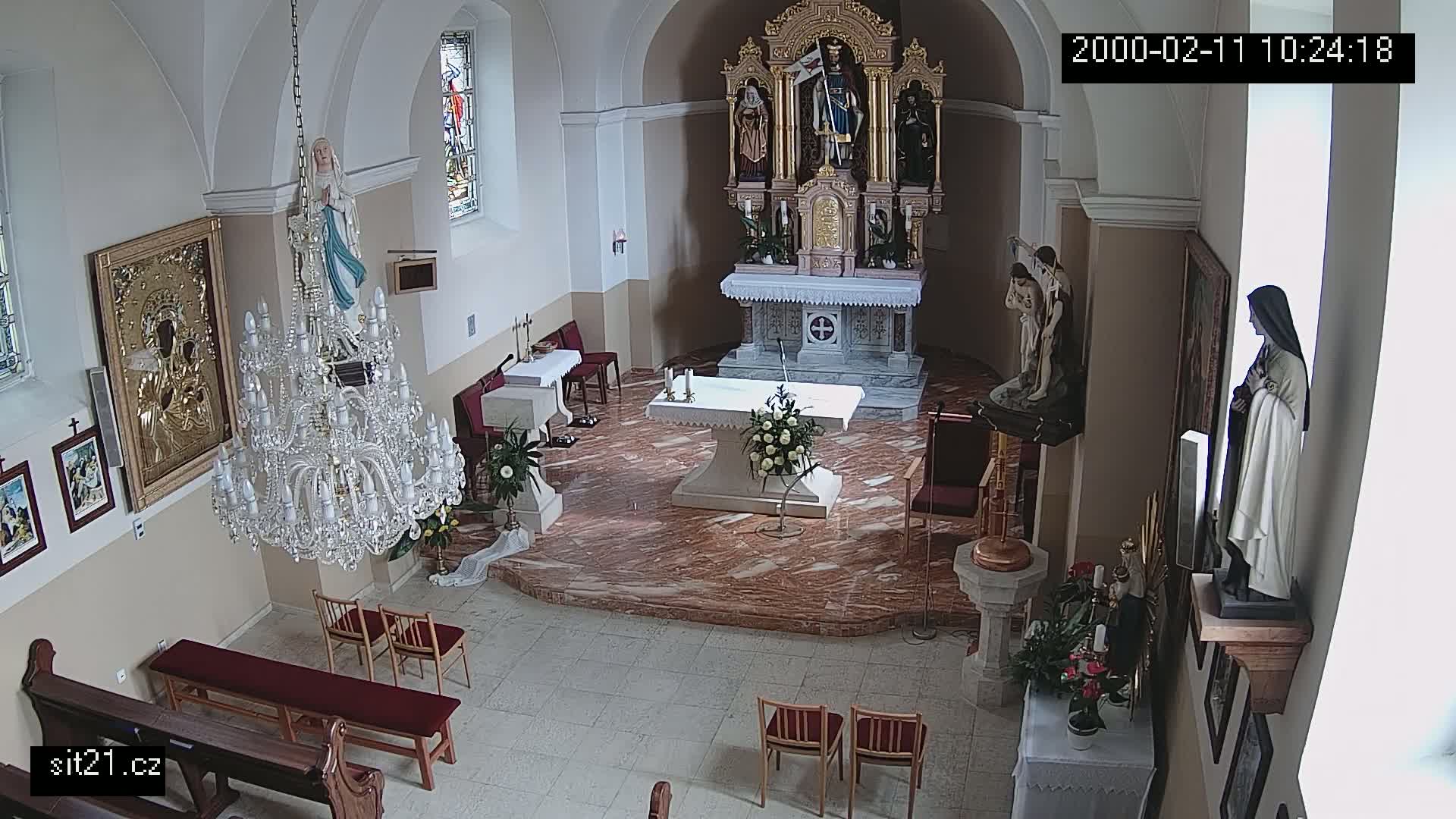 A church interior with an altar, statues, a large chandelier, and pews, showing a marble floor.