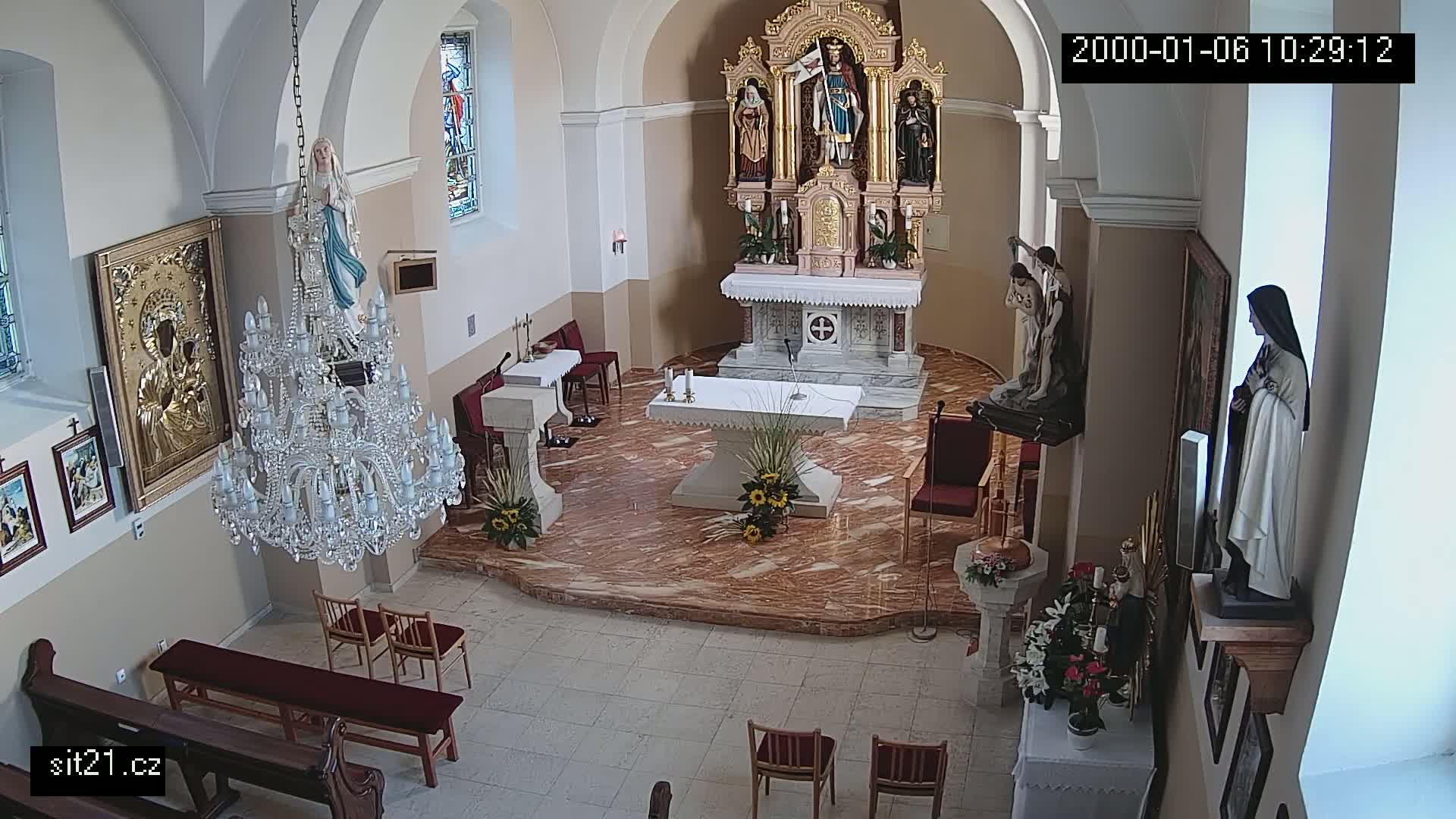 A church interior with an altar, statues, a large chandelier, and pews, showing a marble floor.