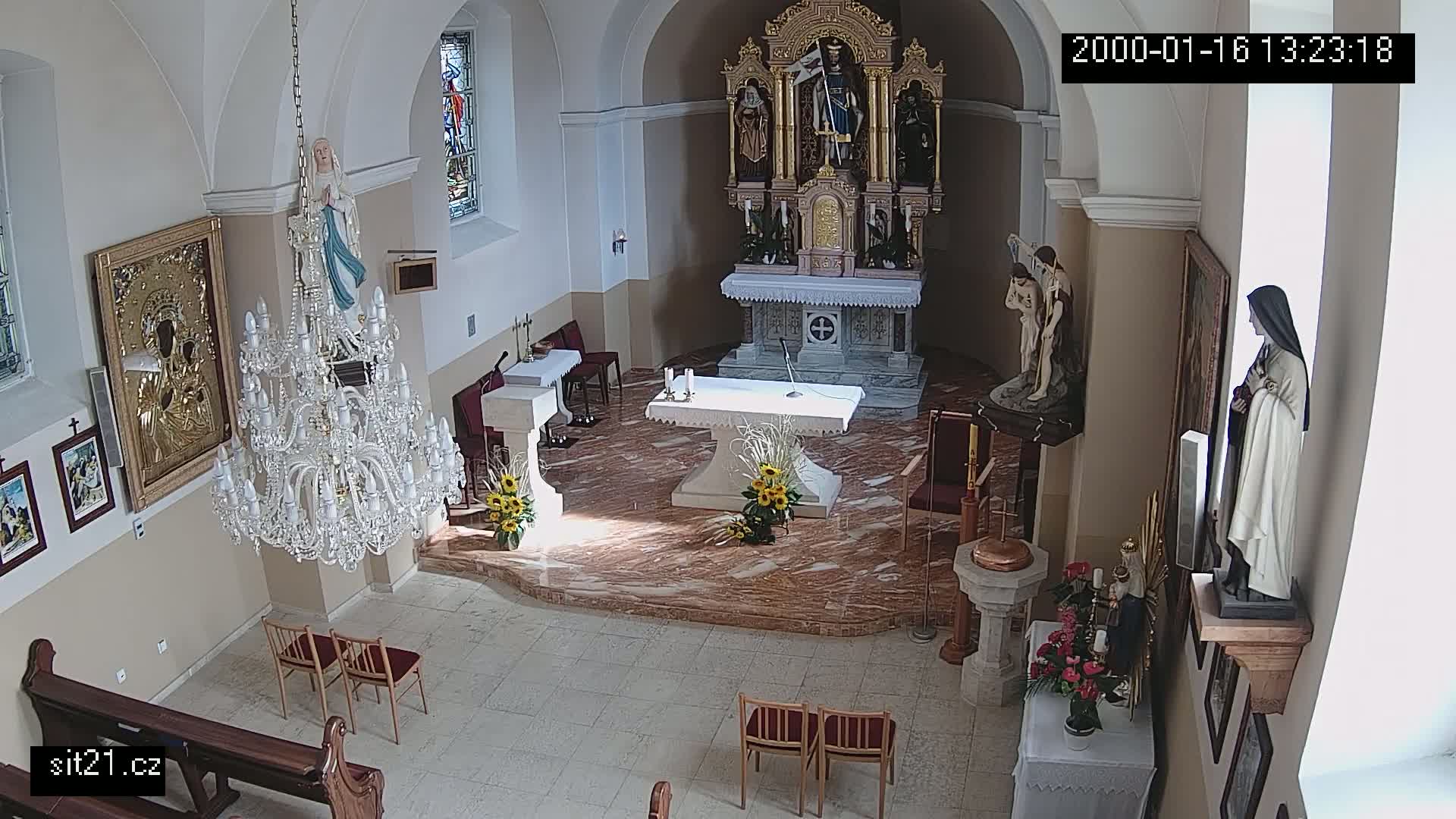 An interior view of a church sanctuary shows an altar, several religious statues and icons, a large crystal chandelier, and a baptismal font.