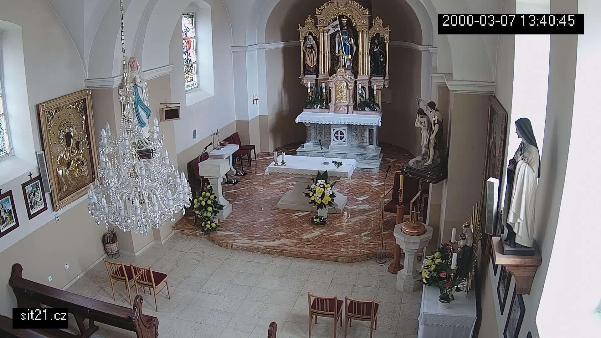 An interior view of a church sanctuary shows an altar, several religious statues and icons, a large crystal chandelier, and a baptismal font.
