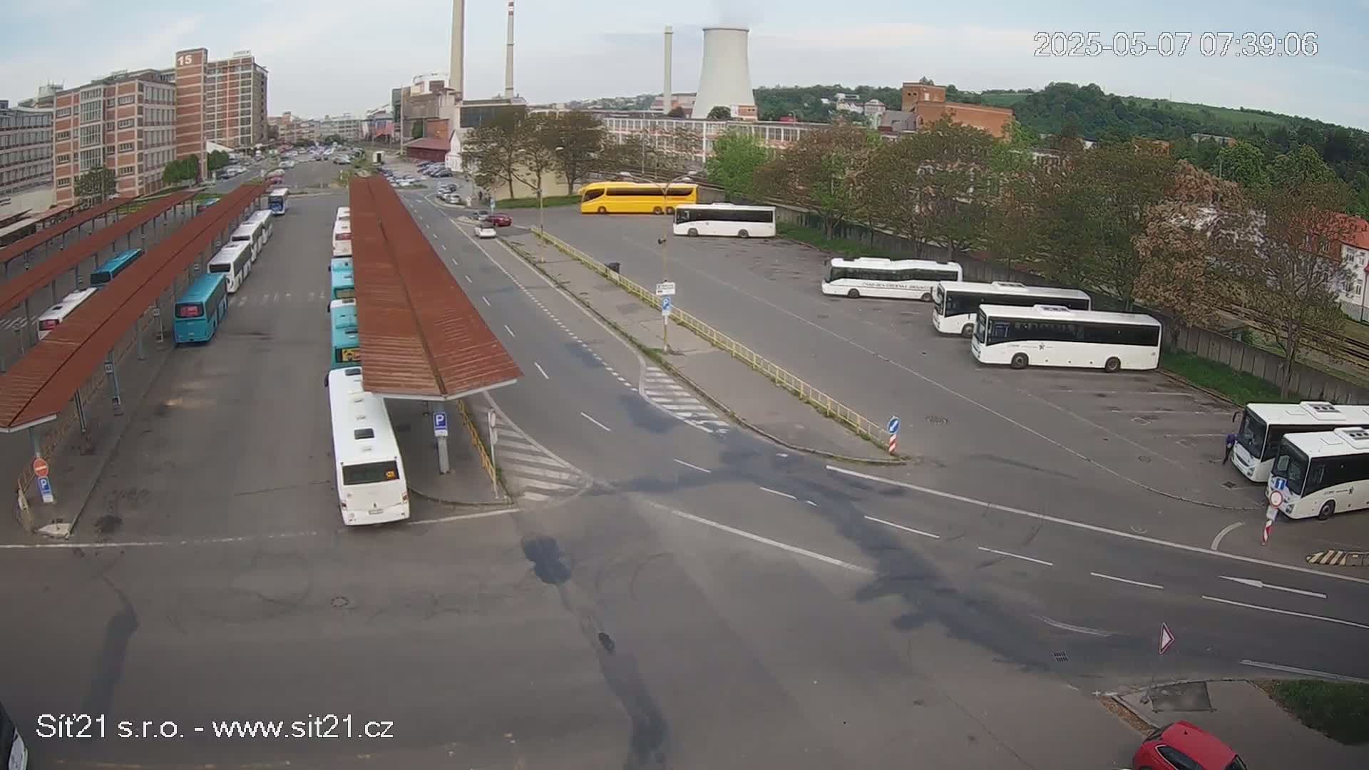 A bus station with numerous buses parked under shelters and in a lot on an overcast day.