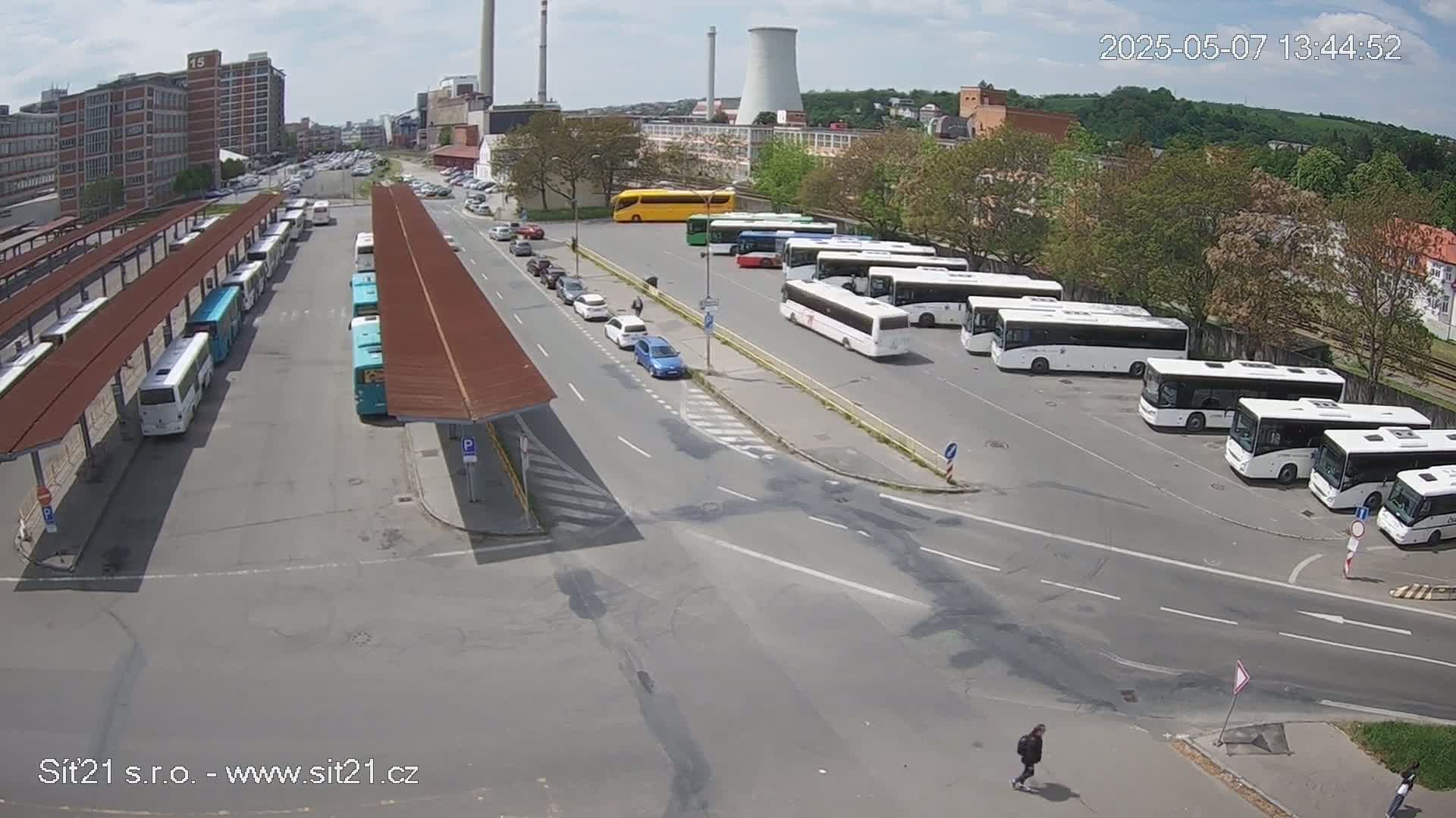 A bus station with many buses parked under covered areas and in an open lot on a partly cloudy day.