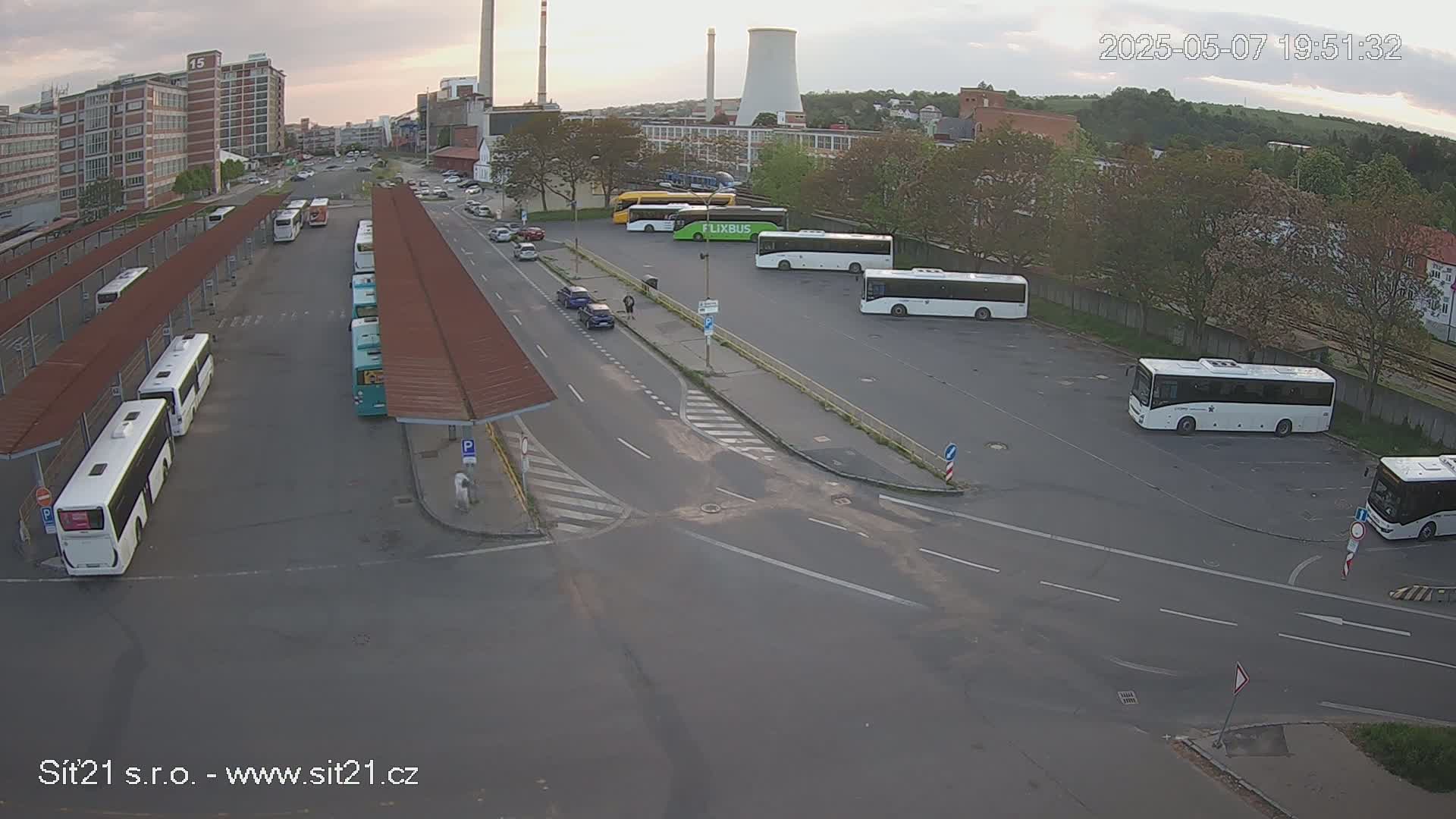 A bus station with numerous buses parked under covered areas and in an adjacent lot on an overcast day.