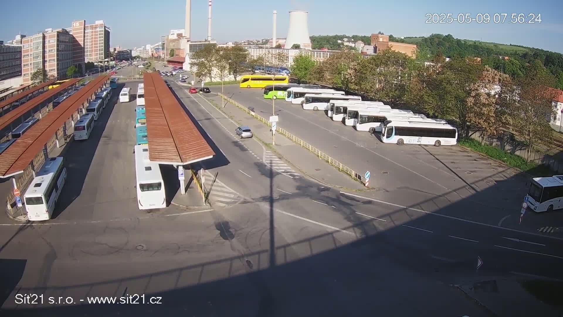A bus station with numerous buses parked under covered shelters and in an adjacent lot on a sunny day.