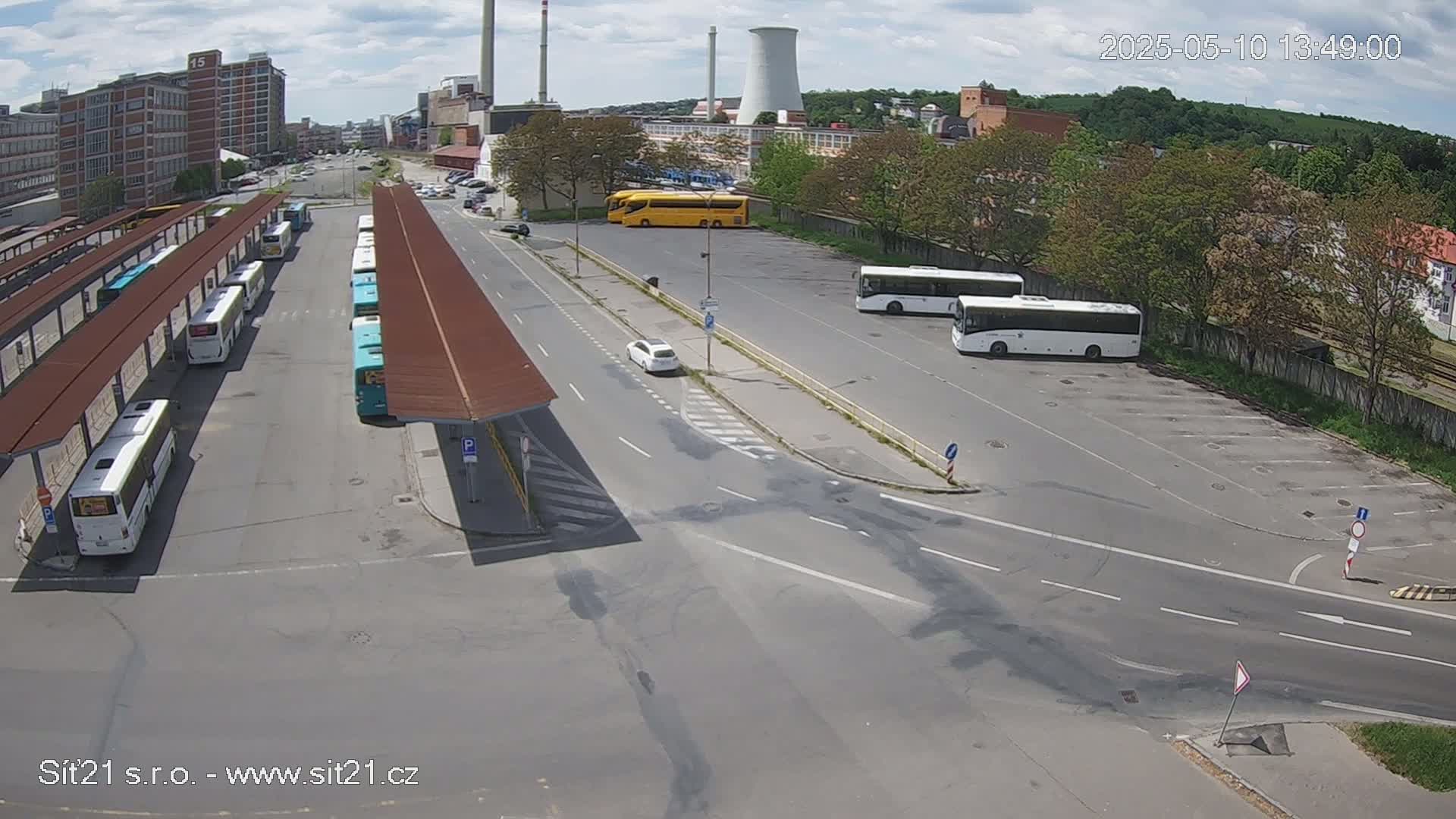 A bus station with numerous buses parked under shelters, additional buses in a nearby lot, and a few cars, all under partly cloudy skies.