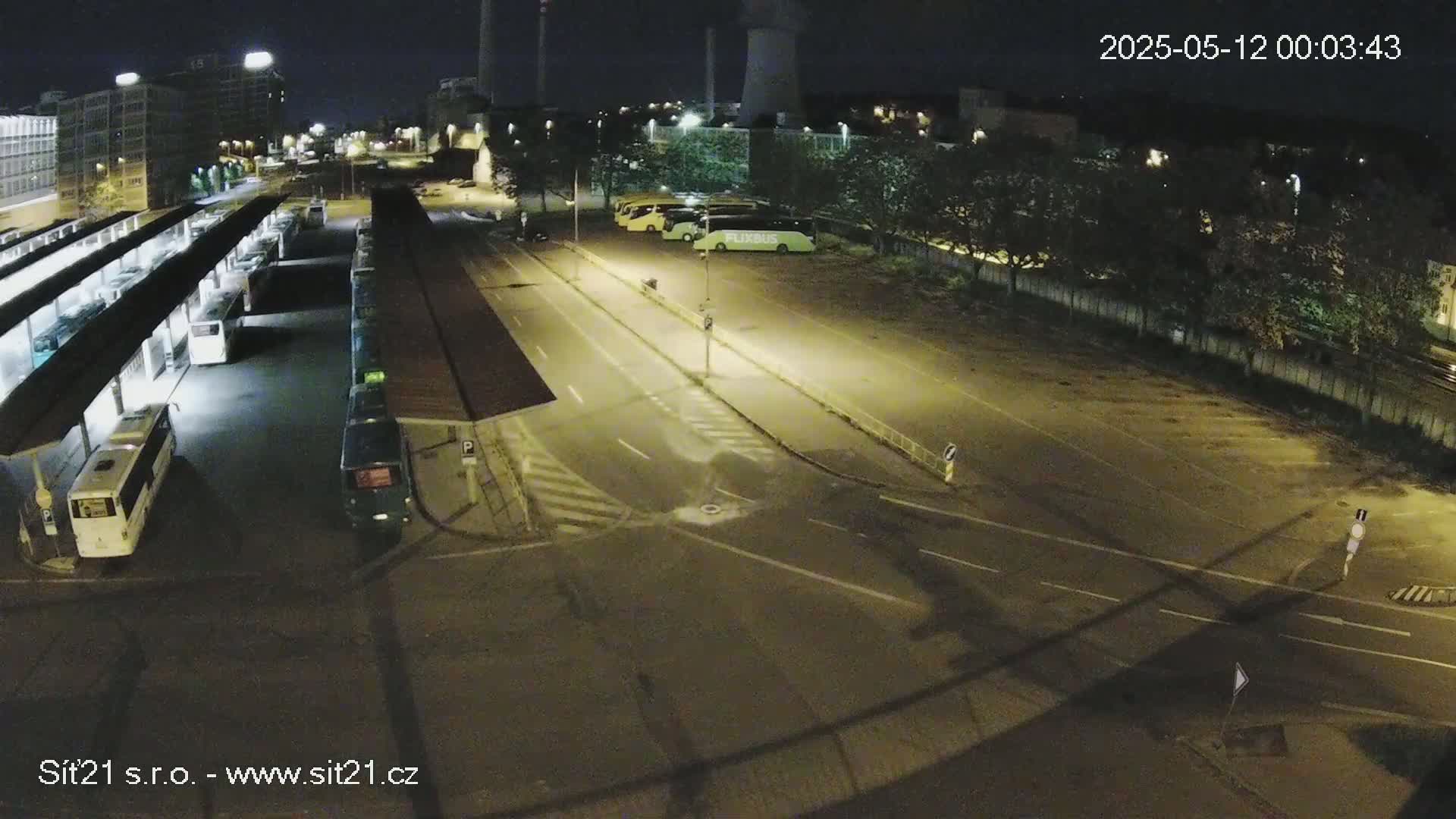 A nighttime, high-angle view of a bus station with several buses parked under shelters and in a nearby lot.