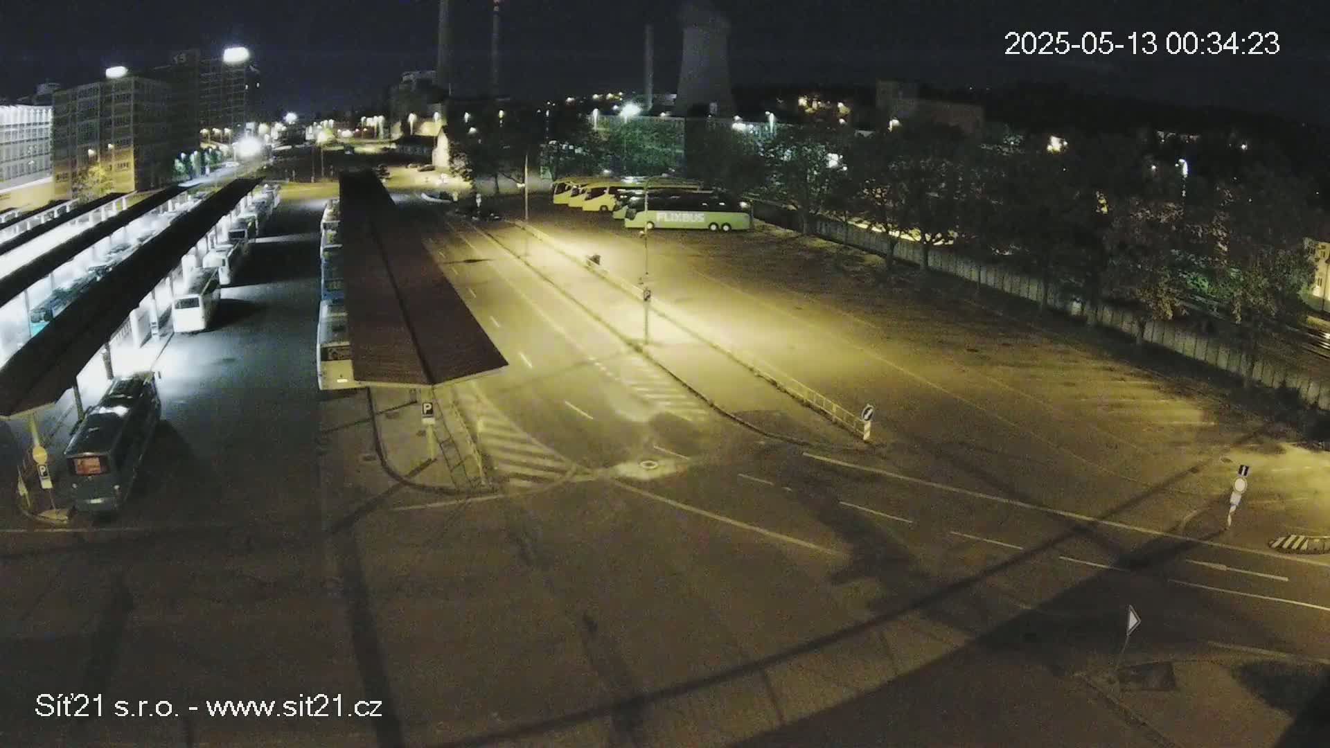 A nighttime, high-angle view of a bus station with several buses parked under shelters, adjacent to a roadway intersection.