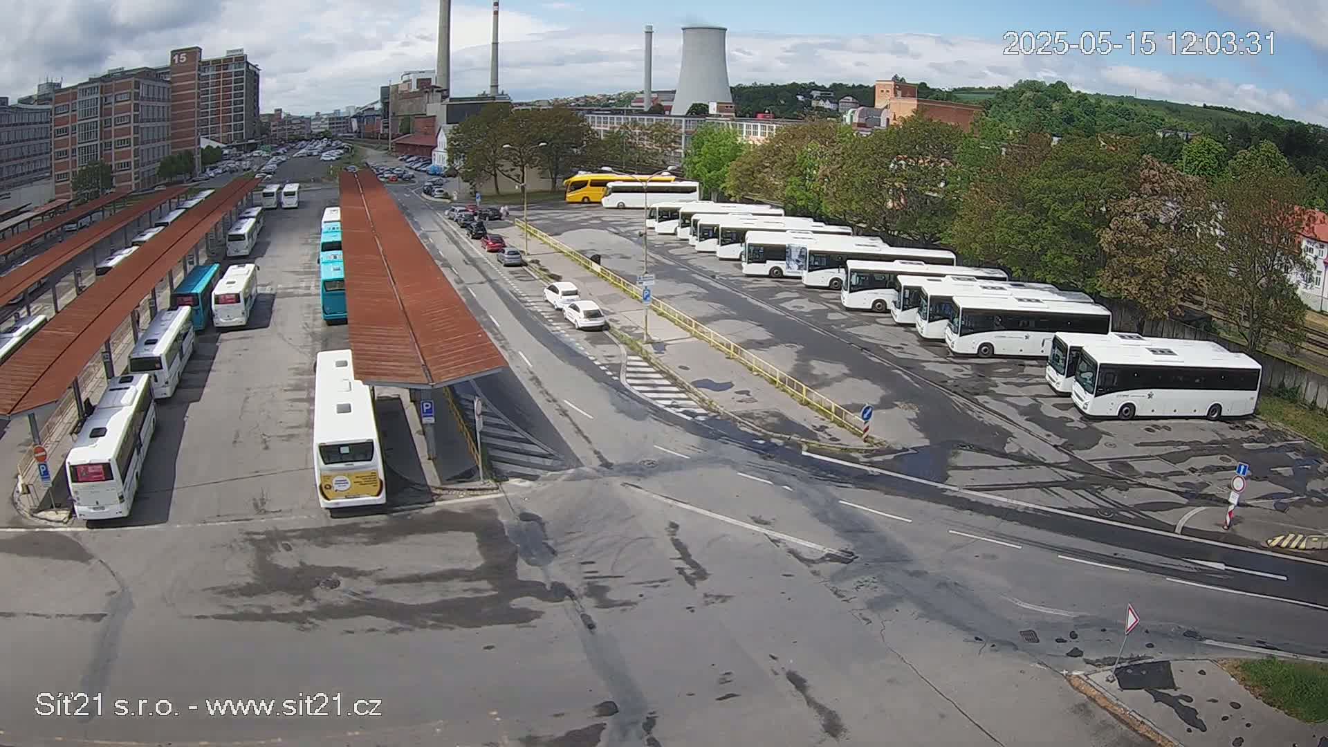 A bus depot with numerous buses parked under covered shelters and in an open lot, on a partly cloudy day.