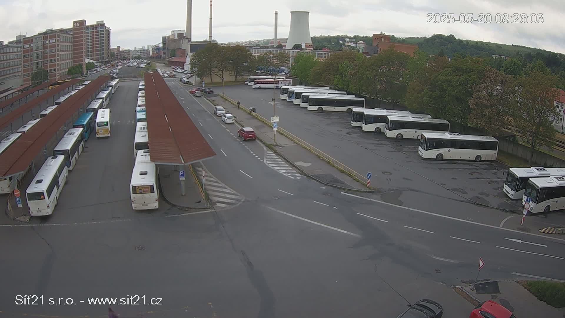 A bus station with numerous buses parked under shelters and in a lot, on an overcast day.