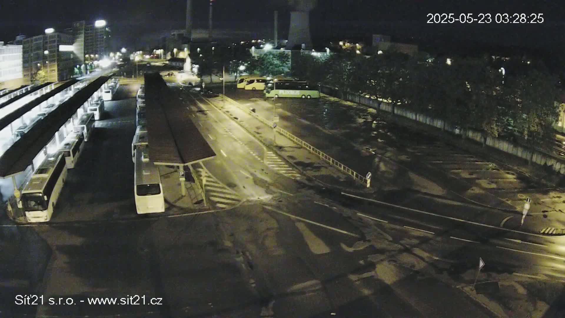 A nighttime aerial view of a bus station with many buses parked under covered shelters, and several more parked in an adjacent lot.