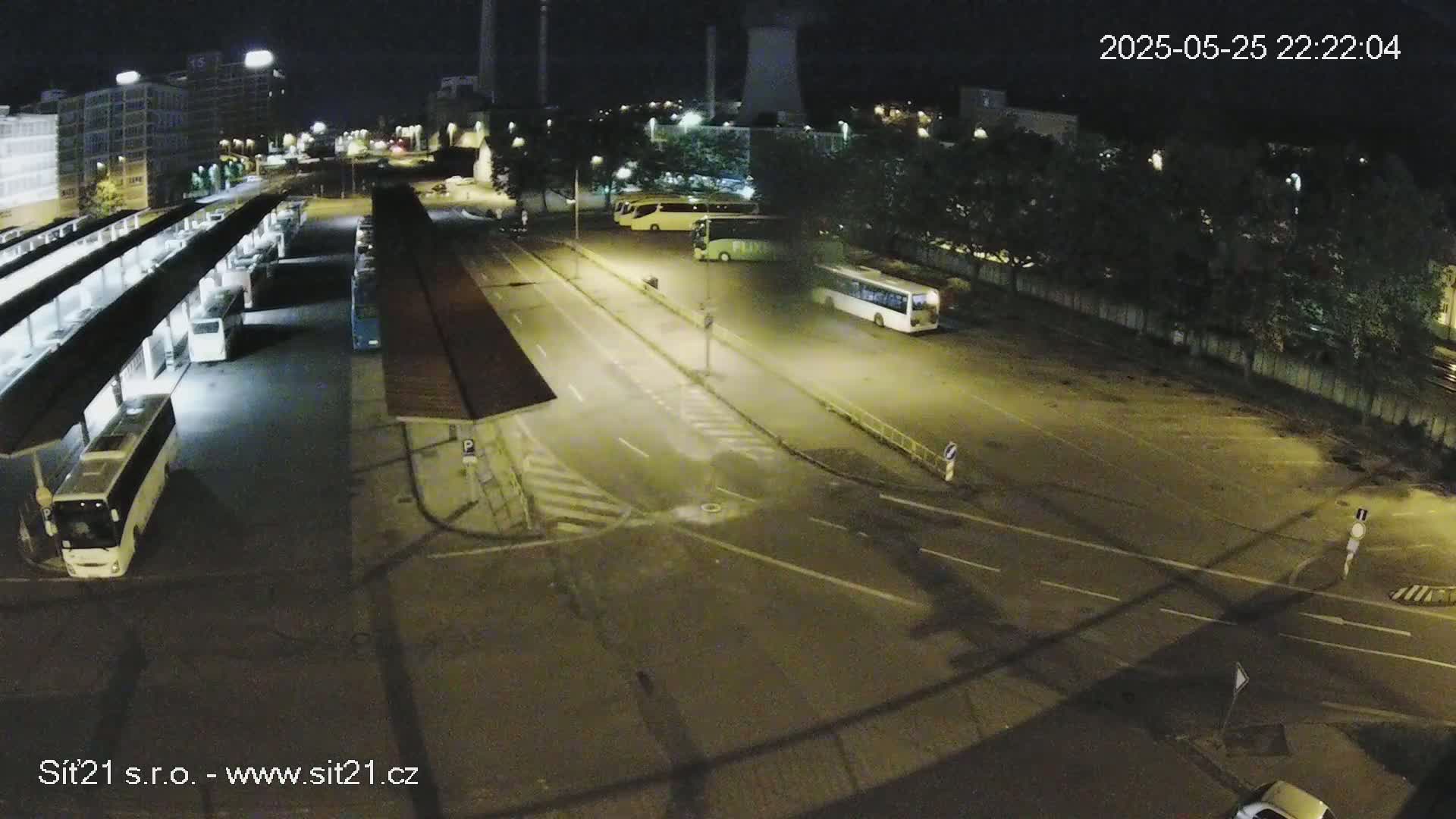A nighttime, high-angle view of a bus station with several buses parked under shelters and in a nearby lot.