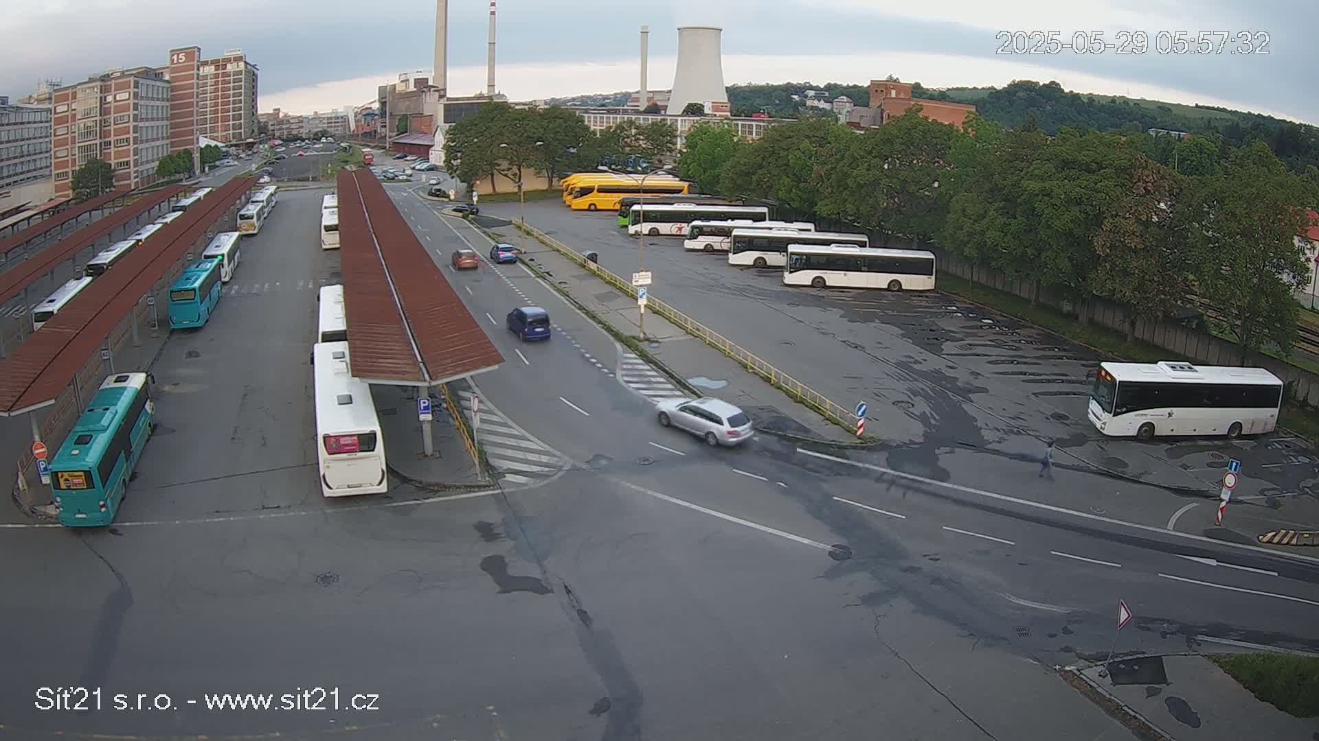 A bus station with numerous buses parked under covered shelters and in a large open-air lot, under an overcast sky.