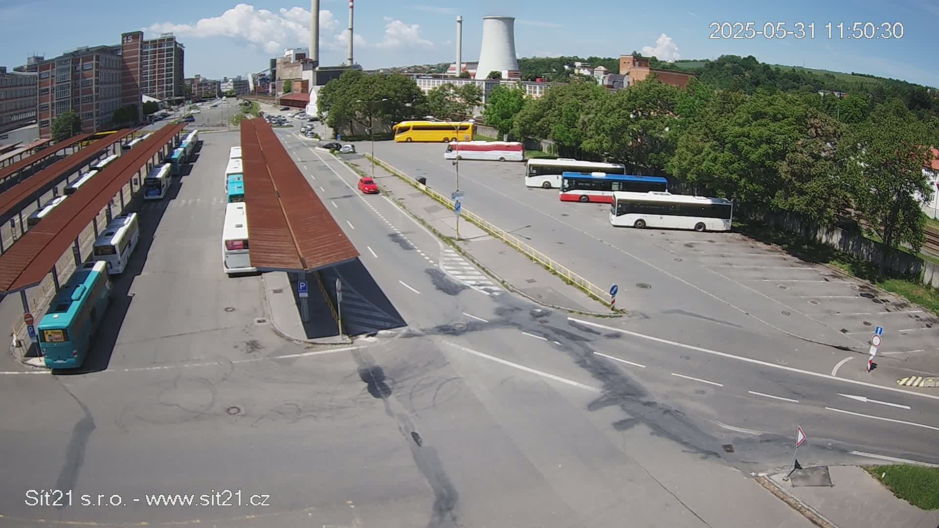 A bus station with numerous buses parked under covered shelters on a sunny day, with additional buses parked in an adjacent lot.