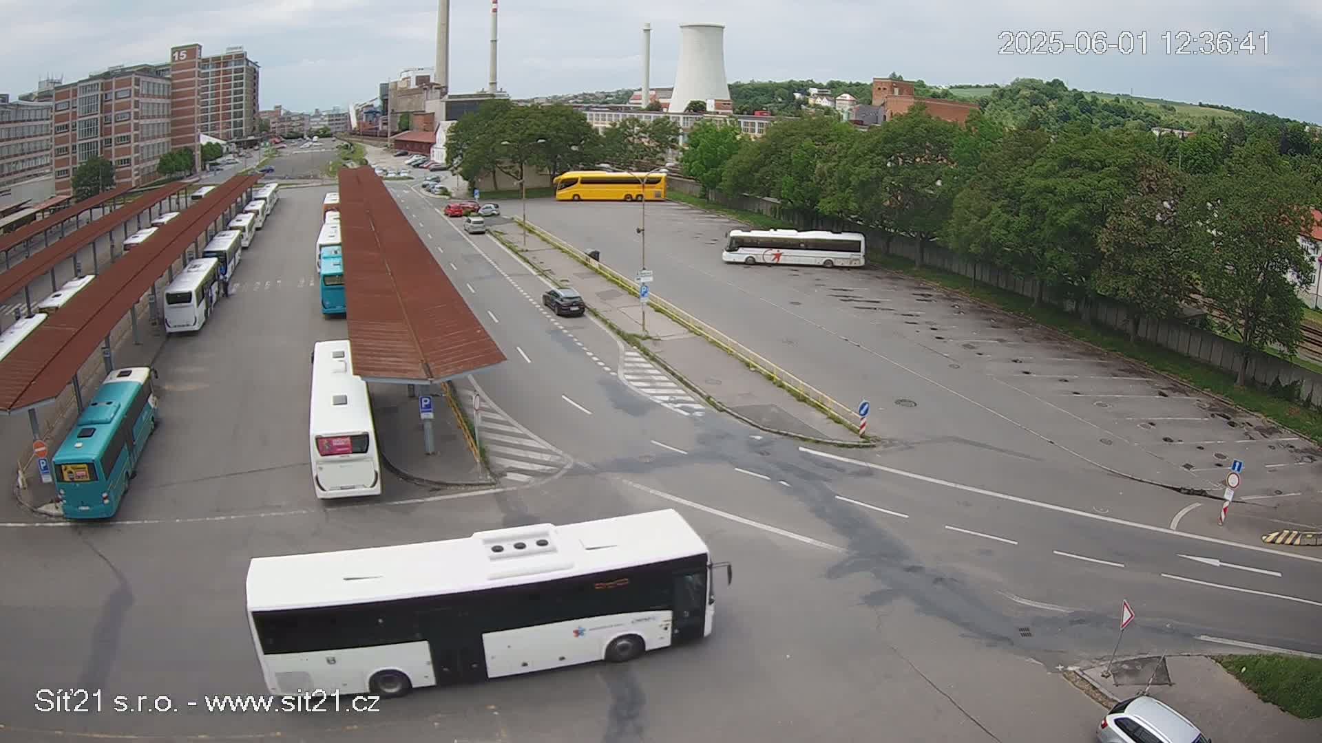 An aerial view shows a bus station with numerous buses parked under shelters,  a few cars in a nearby lot, and an overcast sky.