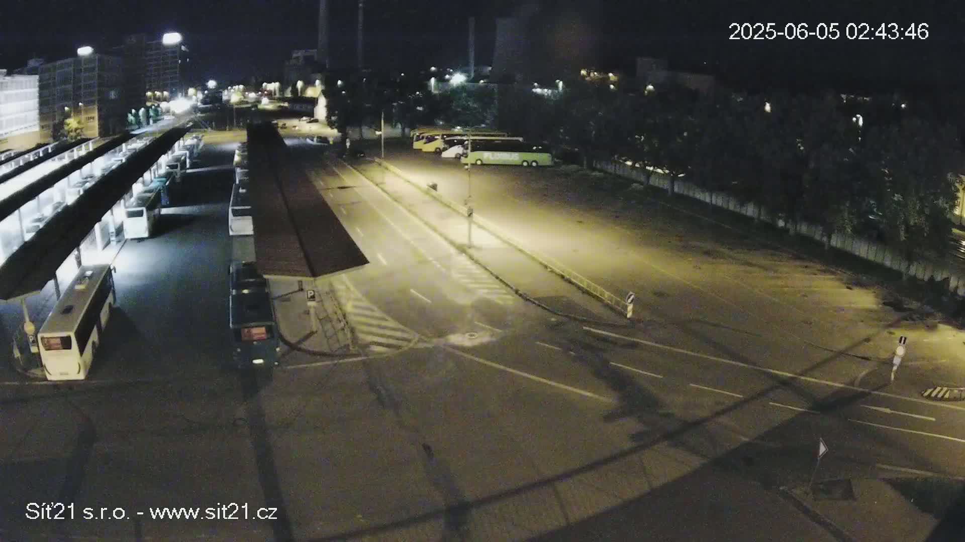 A nighttime view of a bus station with several buses parked under covered shelters and in a nearby lot.