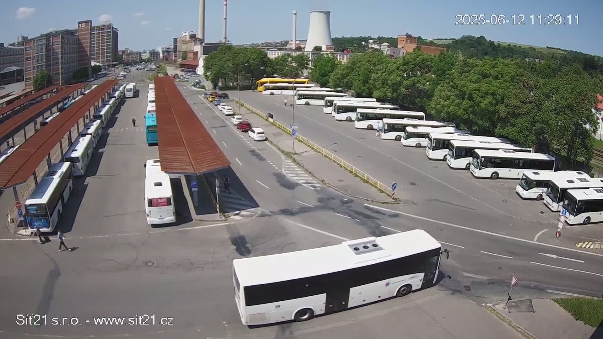 A bus station with numerous buses parked under canopies and in a large parking lot on a sunny day.