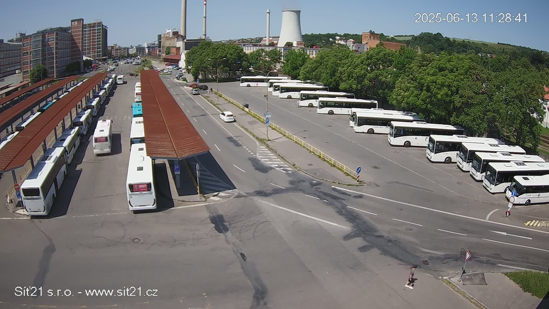 A bus depot with many white buses parked under covered areas and in an open lot on a sunny day.