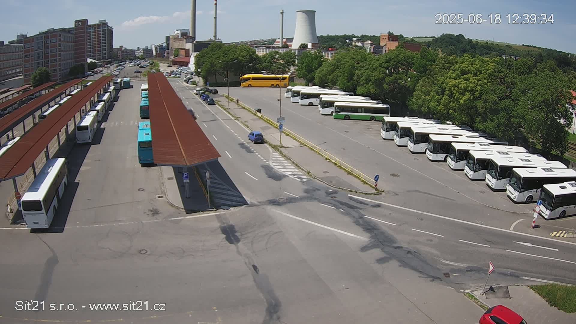 A bus depot with numerous buses parked under covered shelters and in an open lot on a sunny day.