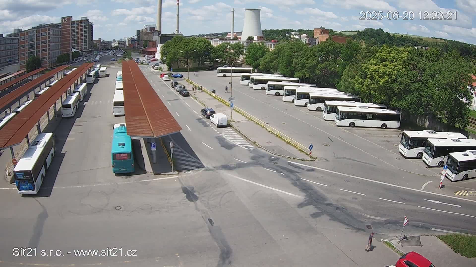 A bus station with numerous buses parked under covered areas and in open lots, on a sunny day.