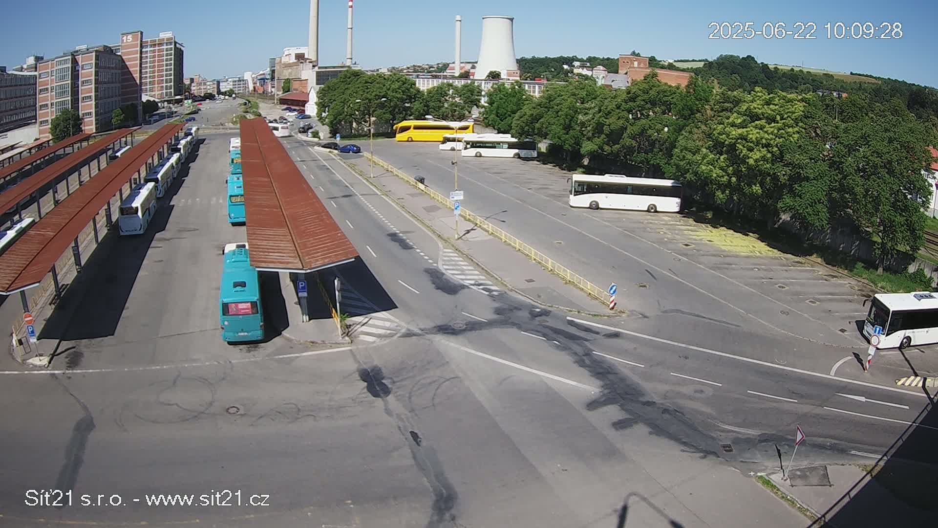 A bus station with numerous buses parked under shelters and in a nearby lot on a sunny day.