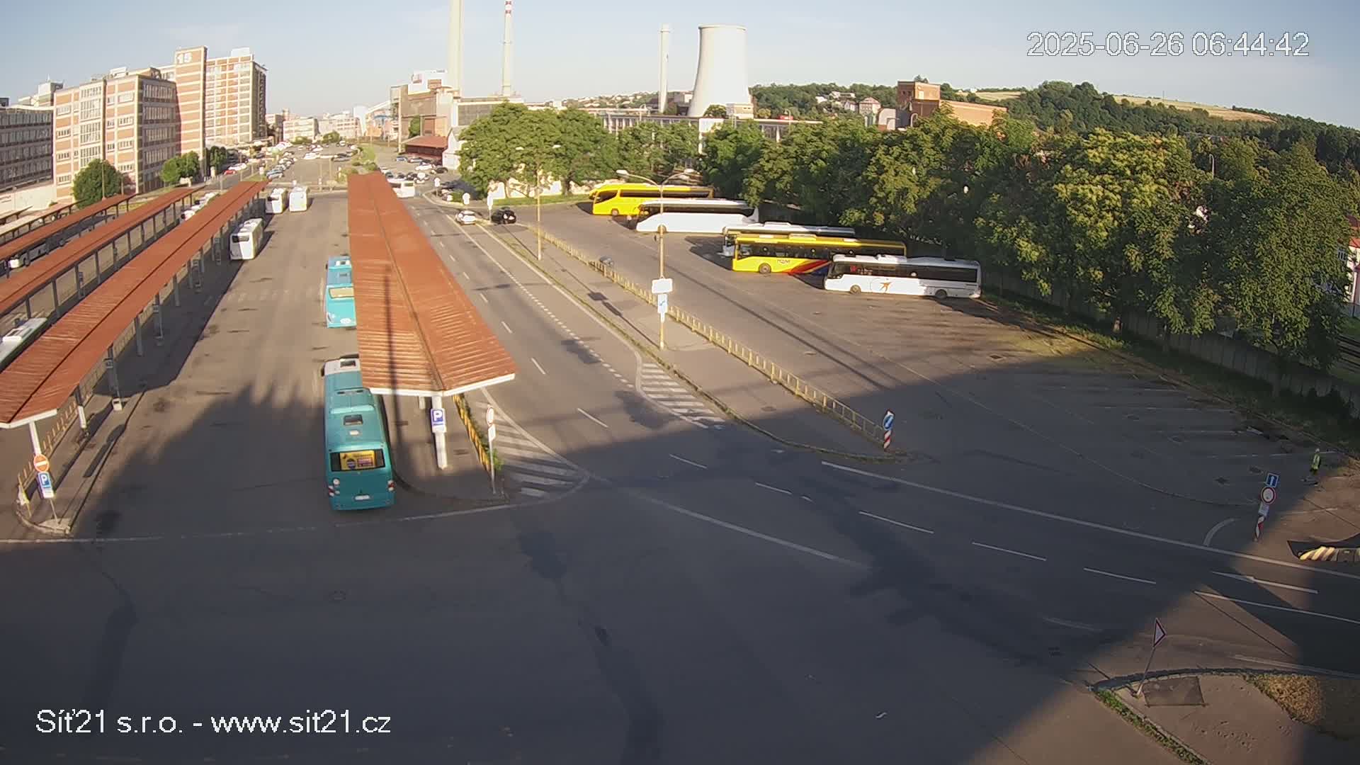 A high-angle, twilight view shows a bus station with numerous buses parked under covered areas, along with additional buses and cars in a nearby parking lot, adjacent to an industrial area.