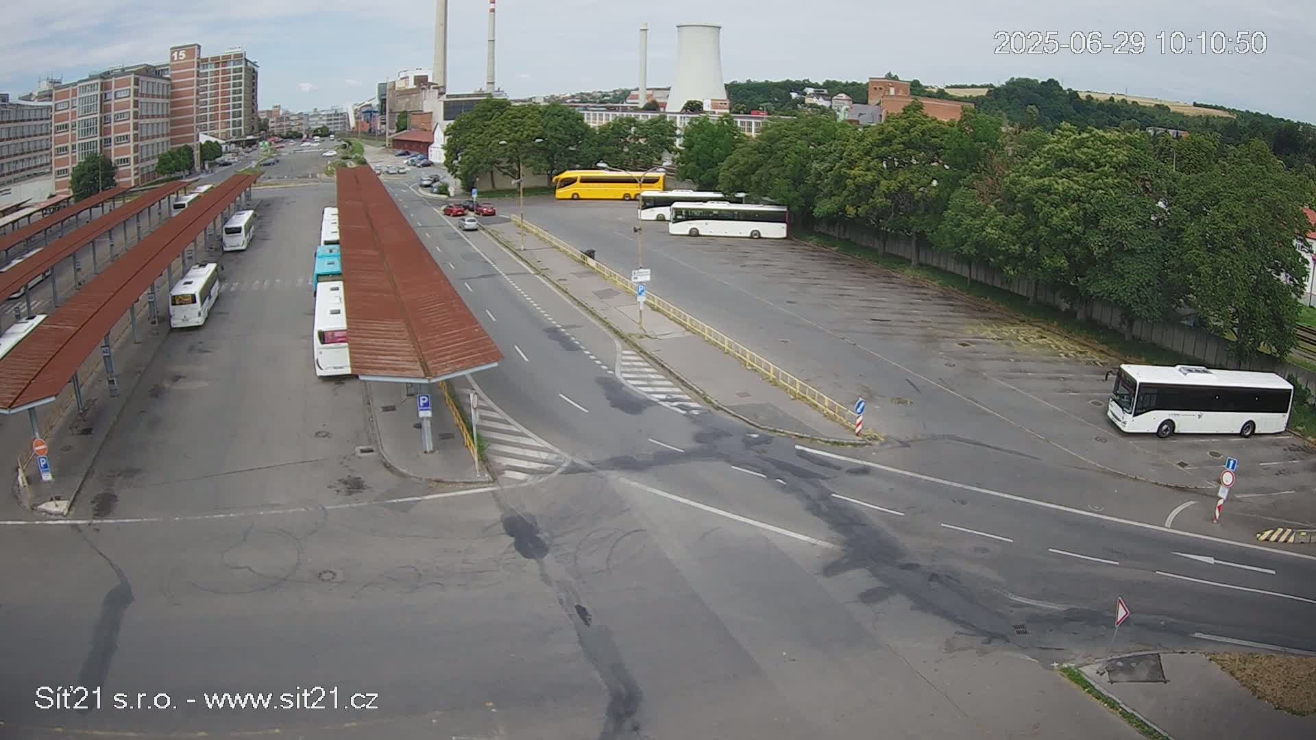 A bus station with several buses parked under shelters and in a nearby lot, on an overcast day.