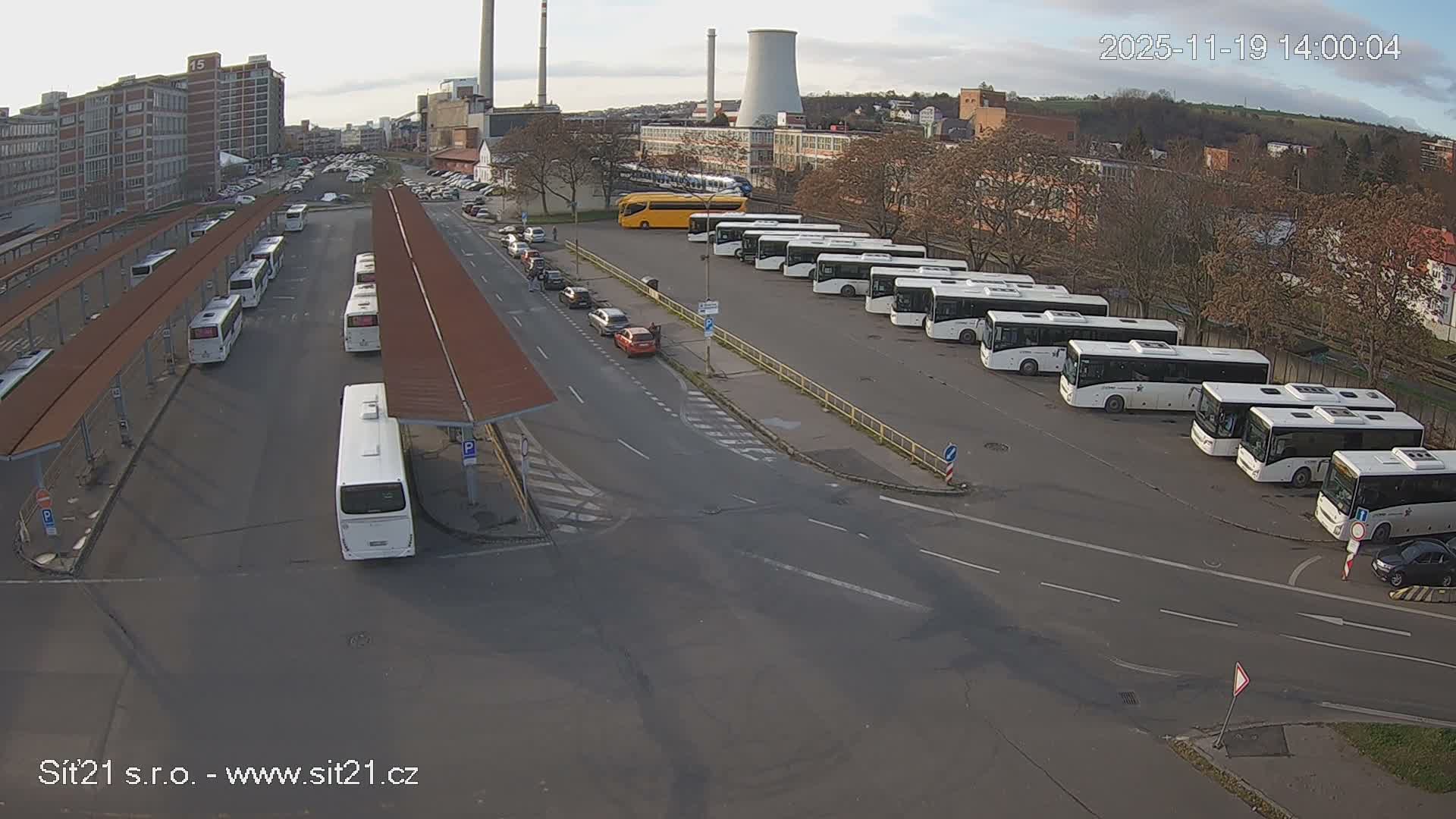 At night, a bus station with numerous buses parked under shelters and a few in a nearby lot is illuminated.