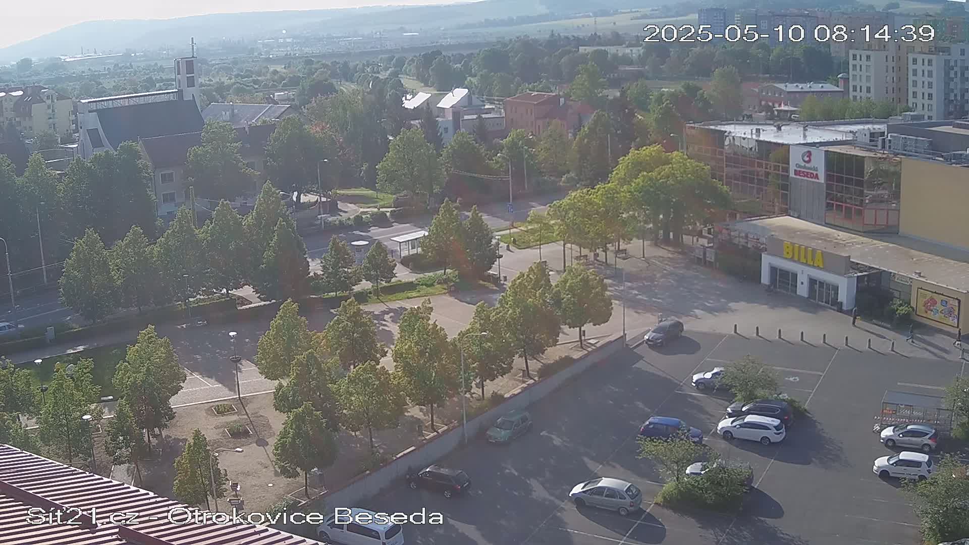 An elevated view of a town square with a church, several buildings, and a parking lot on a sunny day.