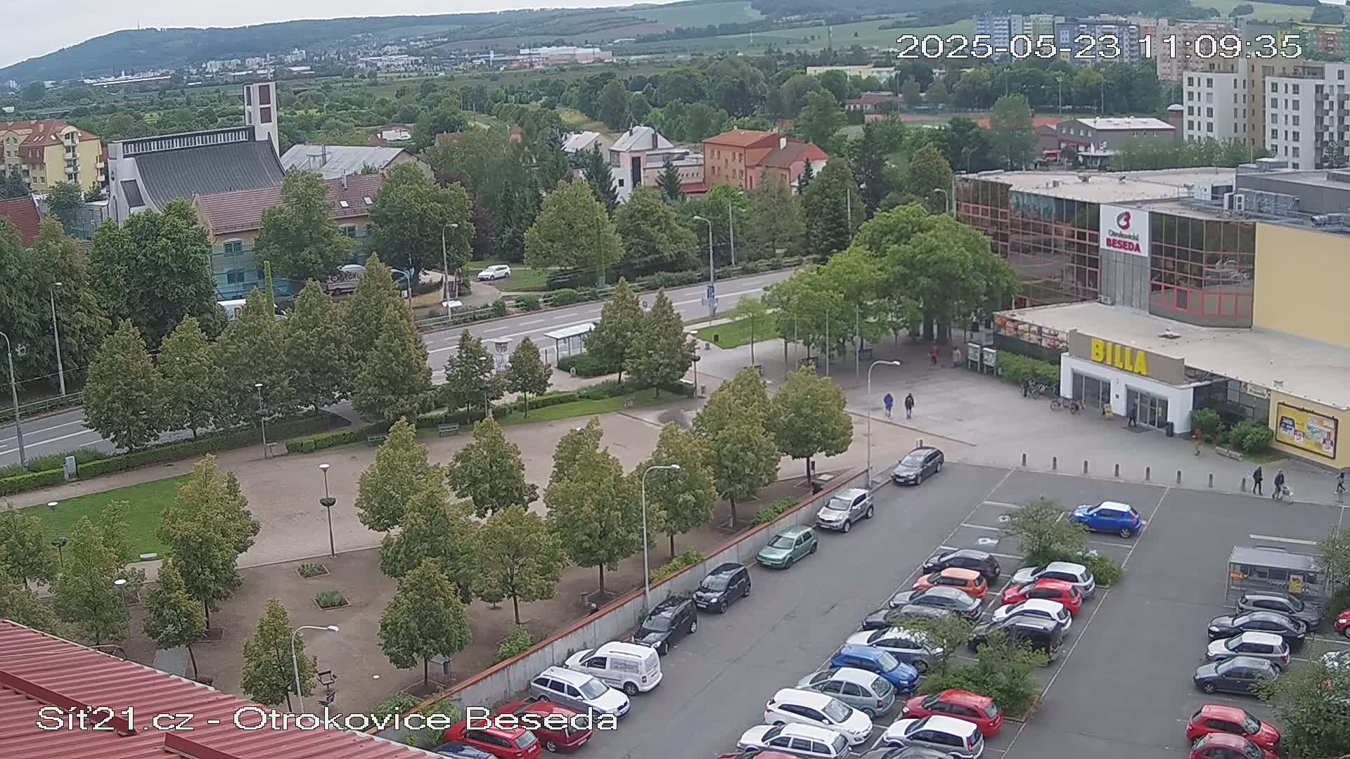 An aerial view of a town square with a church, a large building, and a parking lot, under overcast skies.