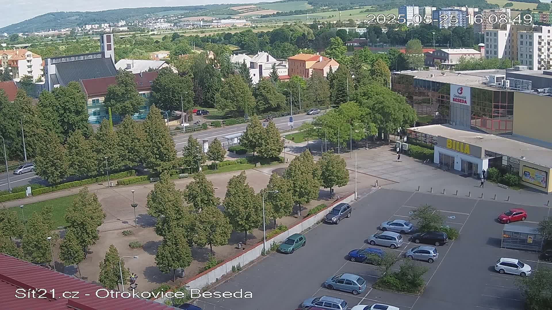 An aerial view shows a town square with a church, a supermarket, and a parking lot on a sunny day.
