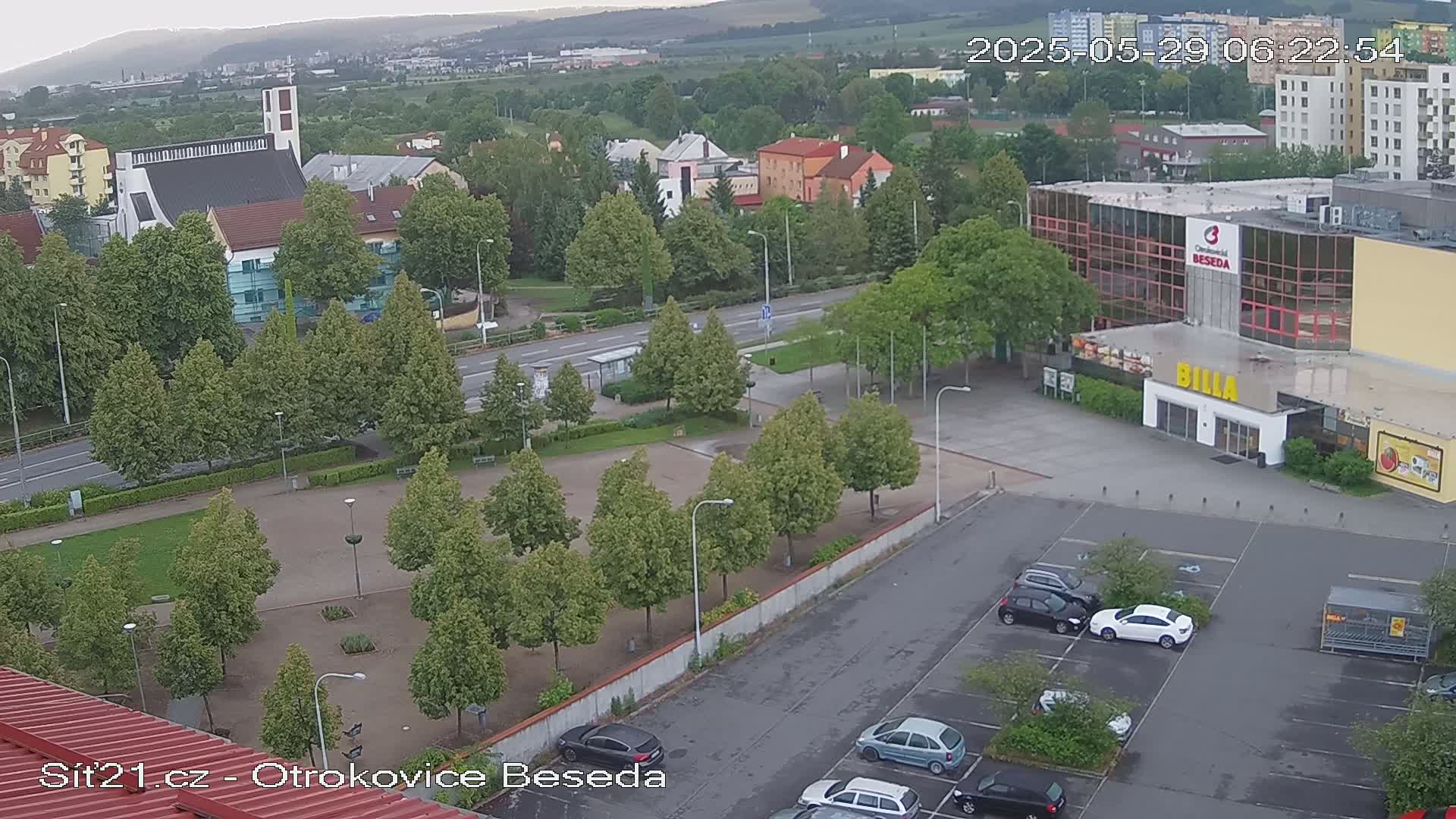 An overcast day reveals a high-angle view of a parking lot, a park with evenly spaced trees, a church, several buildings, and a road.