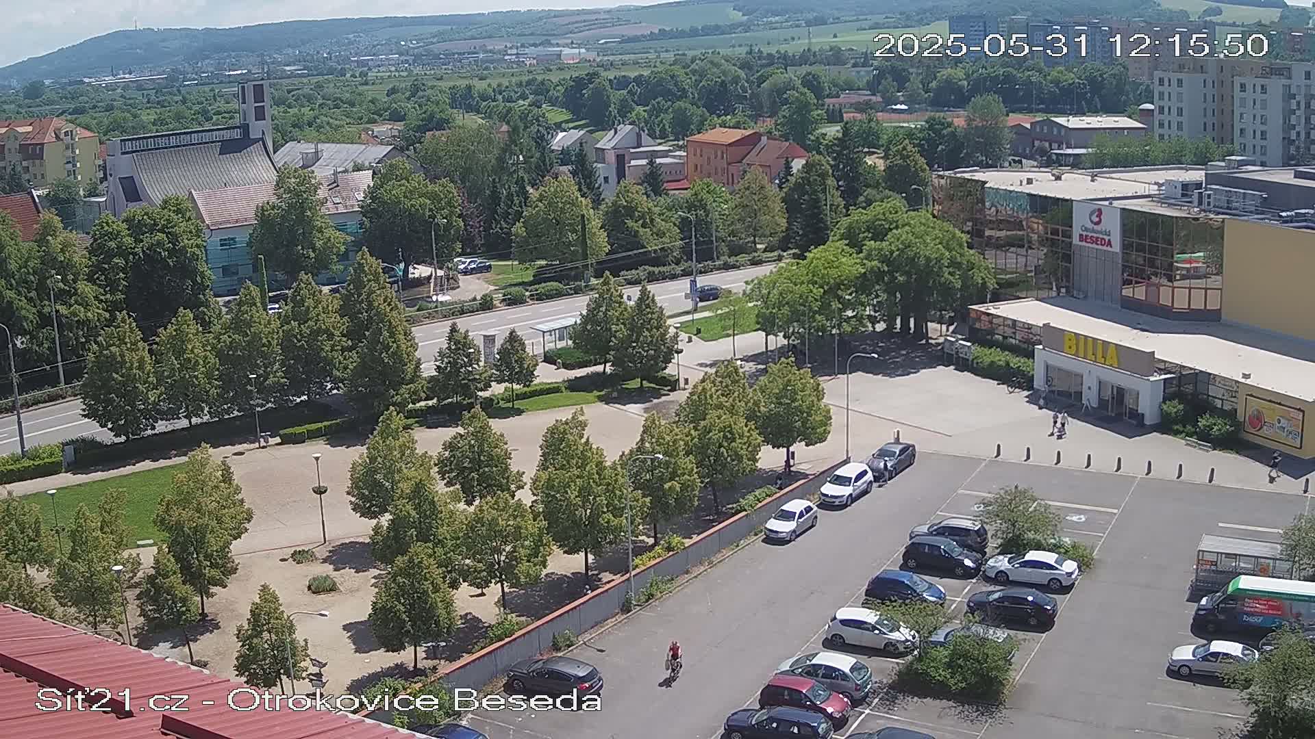 An aerial view of a town square with a church, shops, and a parking lot on a sunny day.