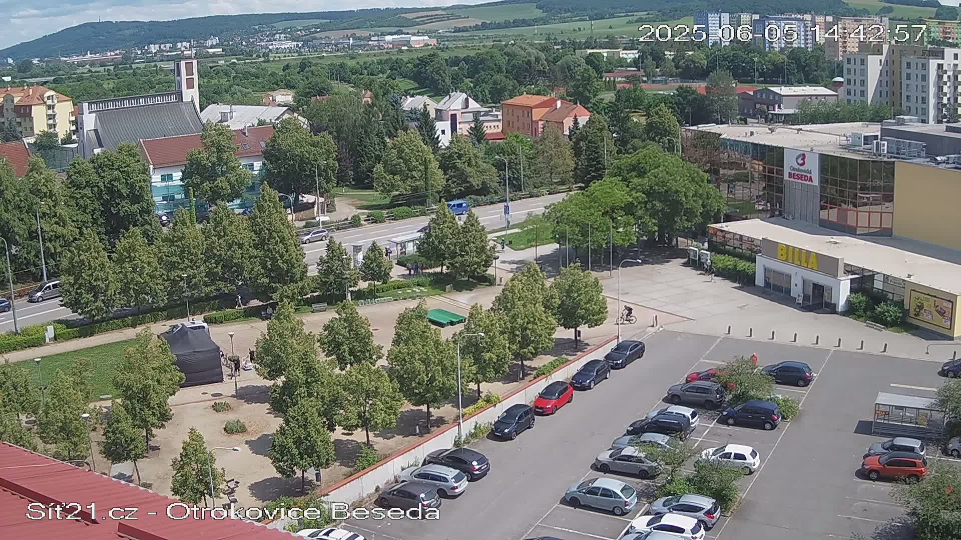 An aerial view of a town square with a parking lot, buildings, and green spaces on a sunny day.