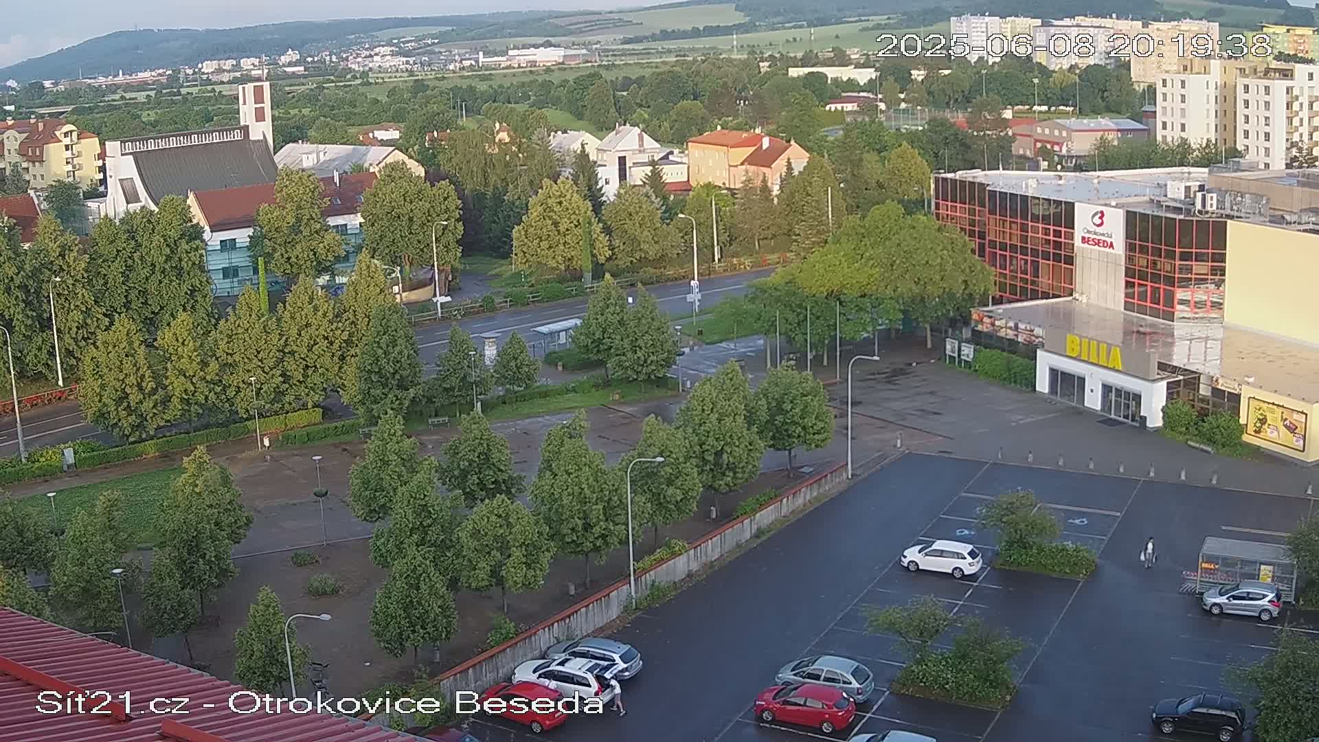 An elevated view shows a town square with a church, several buildings, and a parking lot, all under a mostly clear evening sky.