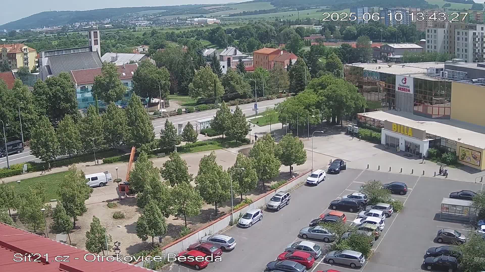 An aerial view of a town square with a church, shops, and a parking lot on a sunny day.