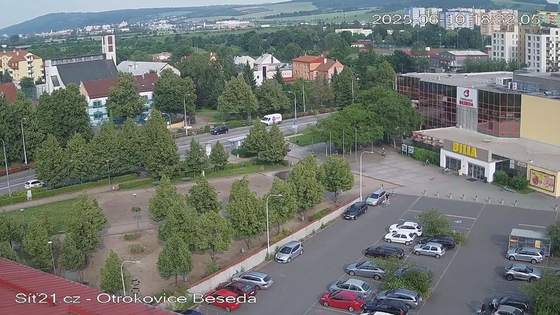 An aerial view shows a parking lot with cars, a grassy area with trees, a church, and a large building with a store.
