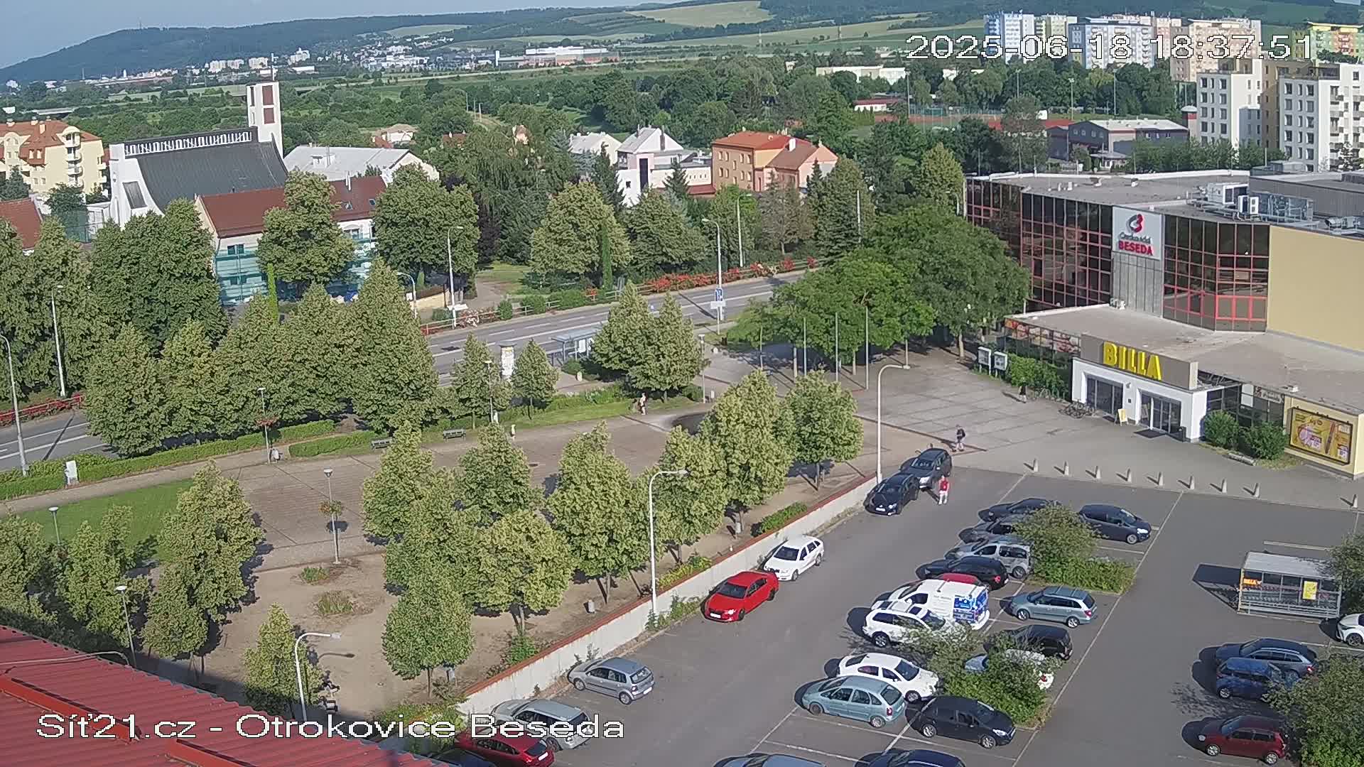 An aerial view of a town square with a church, shopping center, and parking lot on a sunny day.
