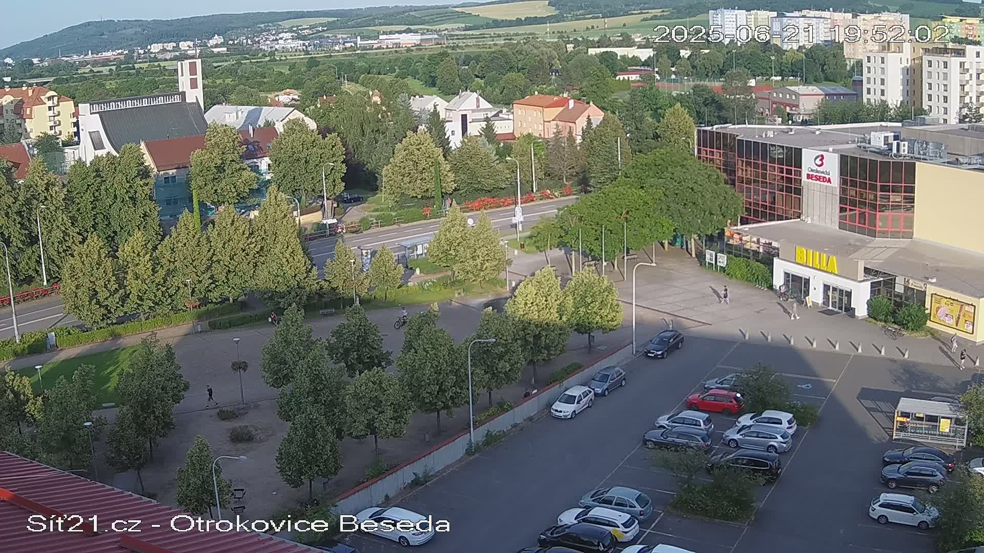 An aerial view shows a town square with a church, a large building, and a parking lot under a clear evening sky.