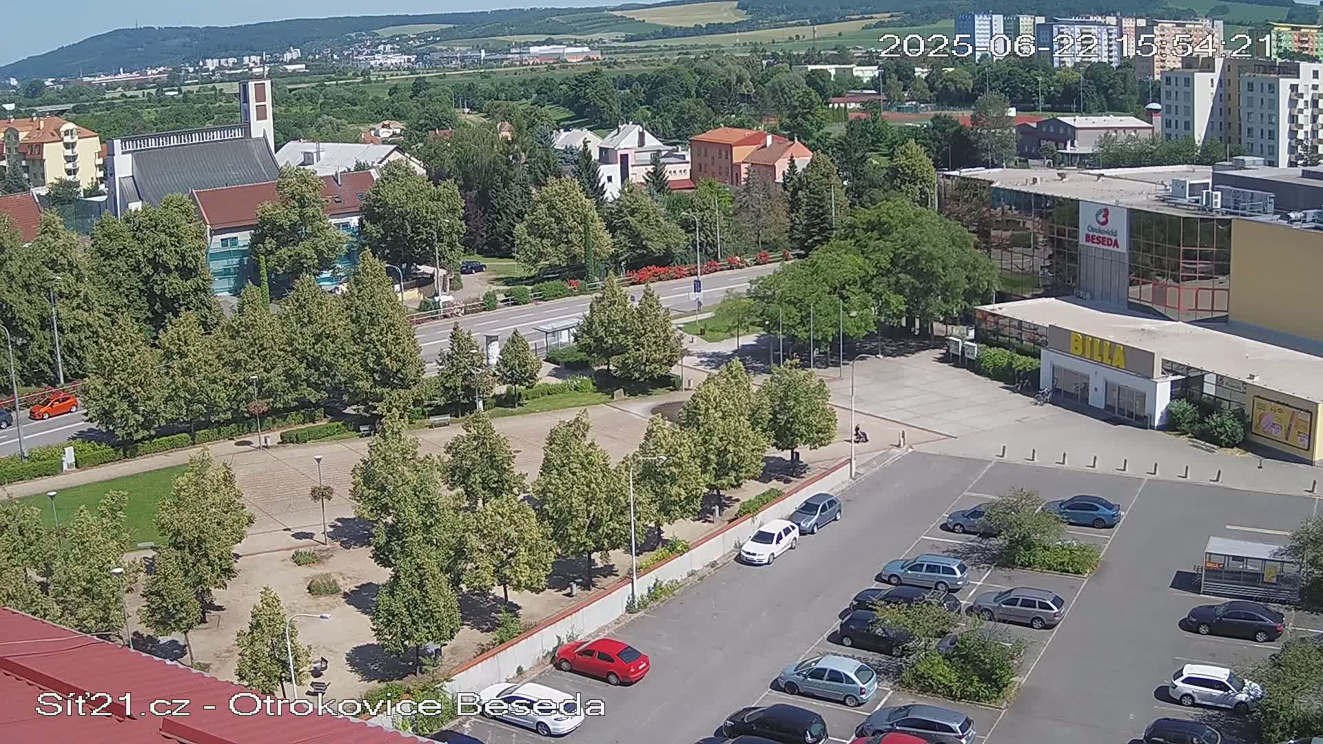 An aerial view of a town square with a church, buildings, trees, and a parking lot on a sunny day.