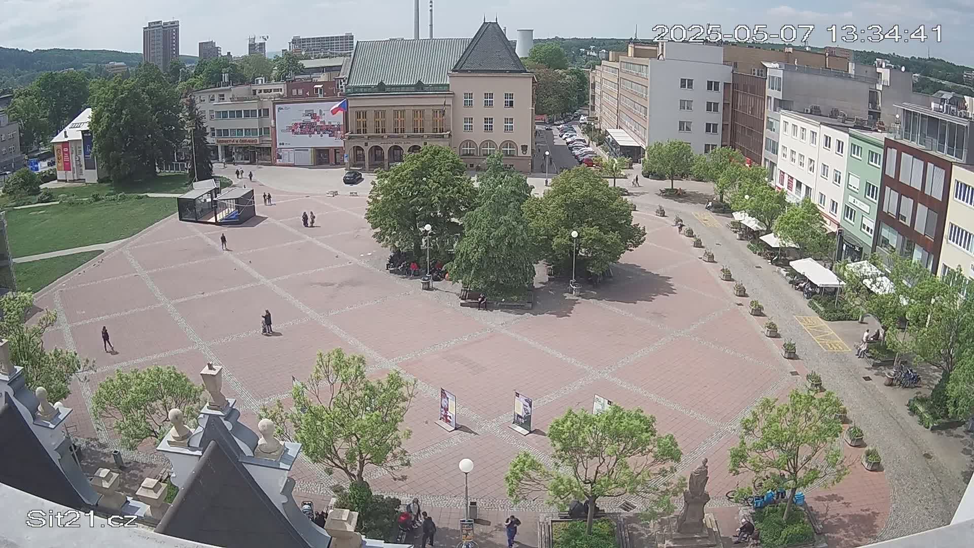 A paved town square with several buildings and trees surrounding it on a sunny day.