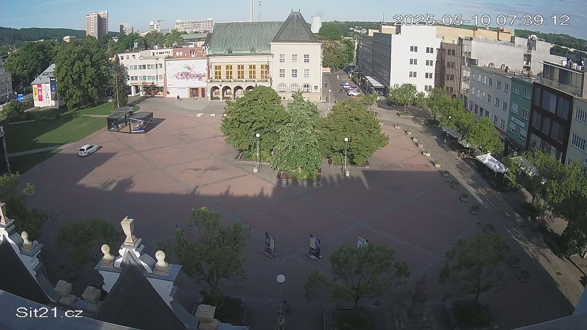 A mostly empty town square with several buildings surrounding it, under a clear, sunny sky.