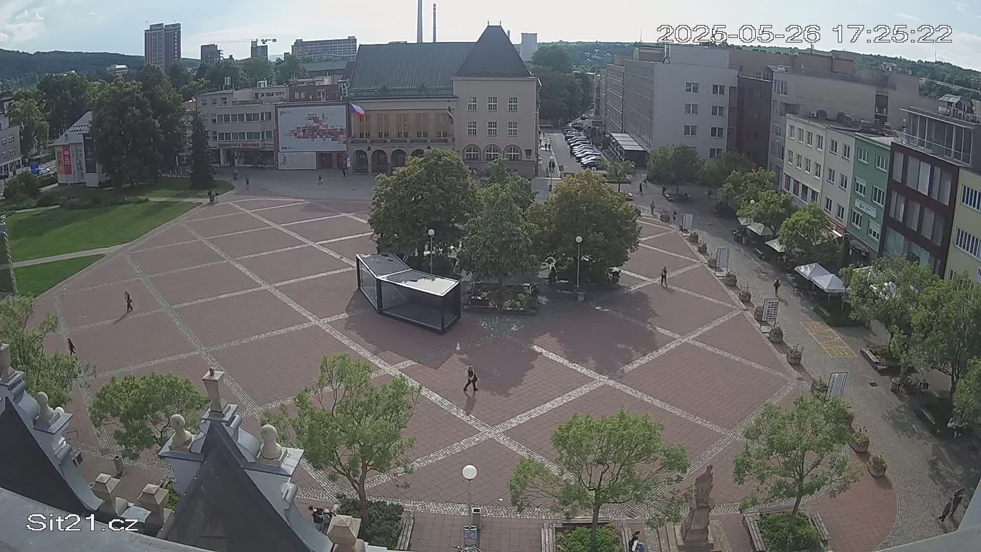 A paved town square with several buildings and trees surrounding it on a sunny day.