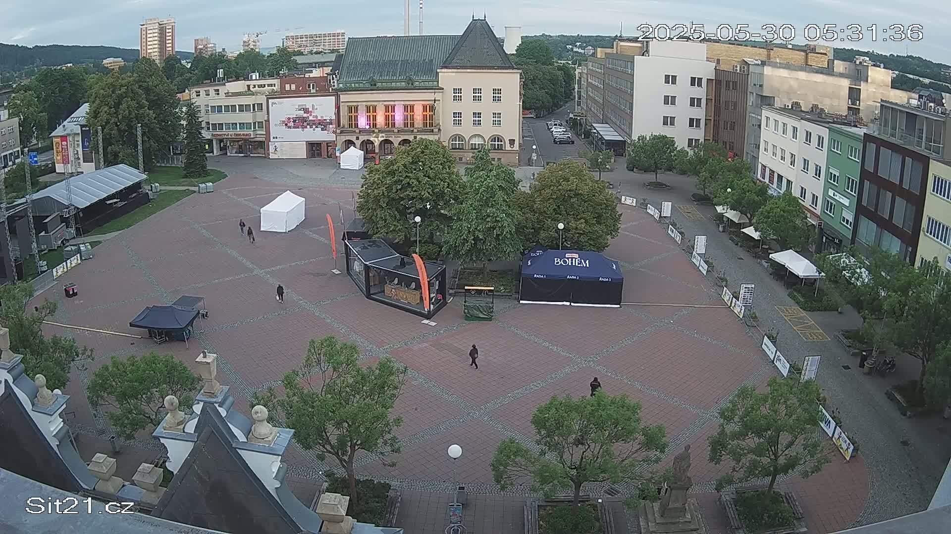 An overcast outdoor town square with several tents, a stage, and a few people sparsely scattered across the paved area.