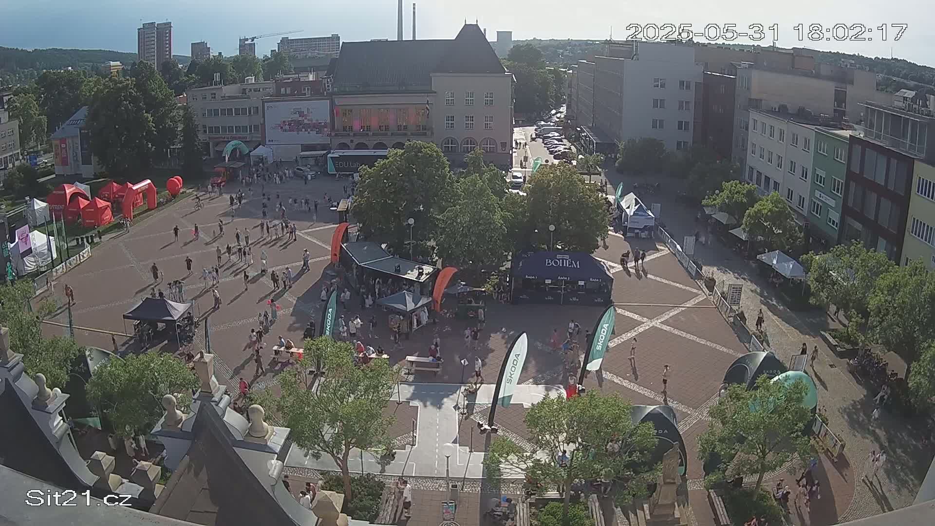 A town square with many people and various booths under a sunny sky.