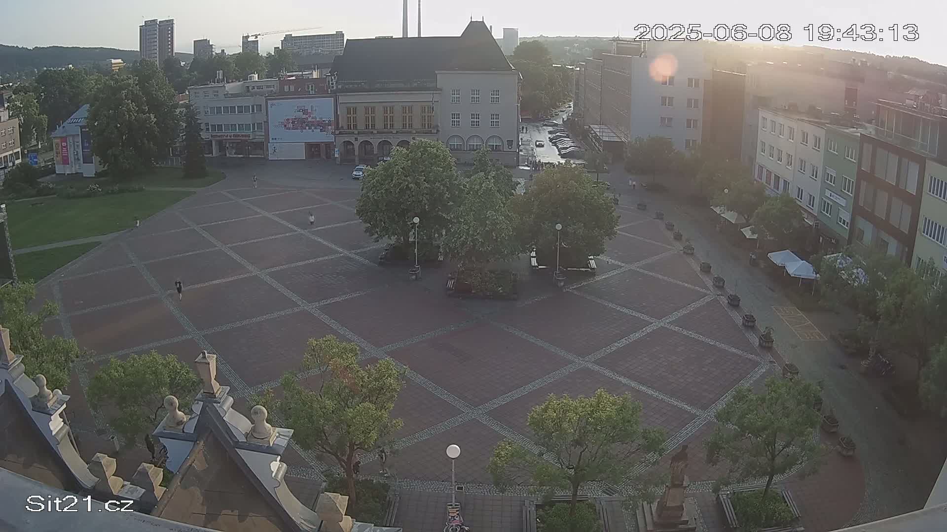 A paved town square with several buildings surrounding it, under a hazy, sunny sky.