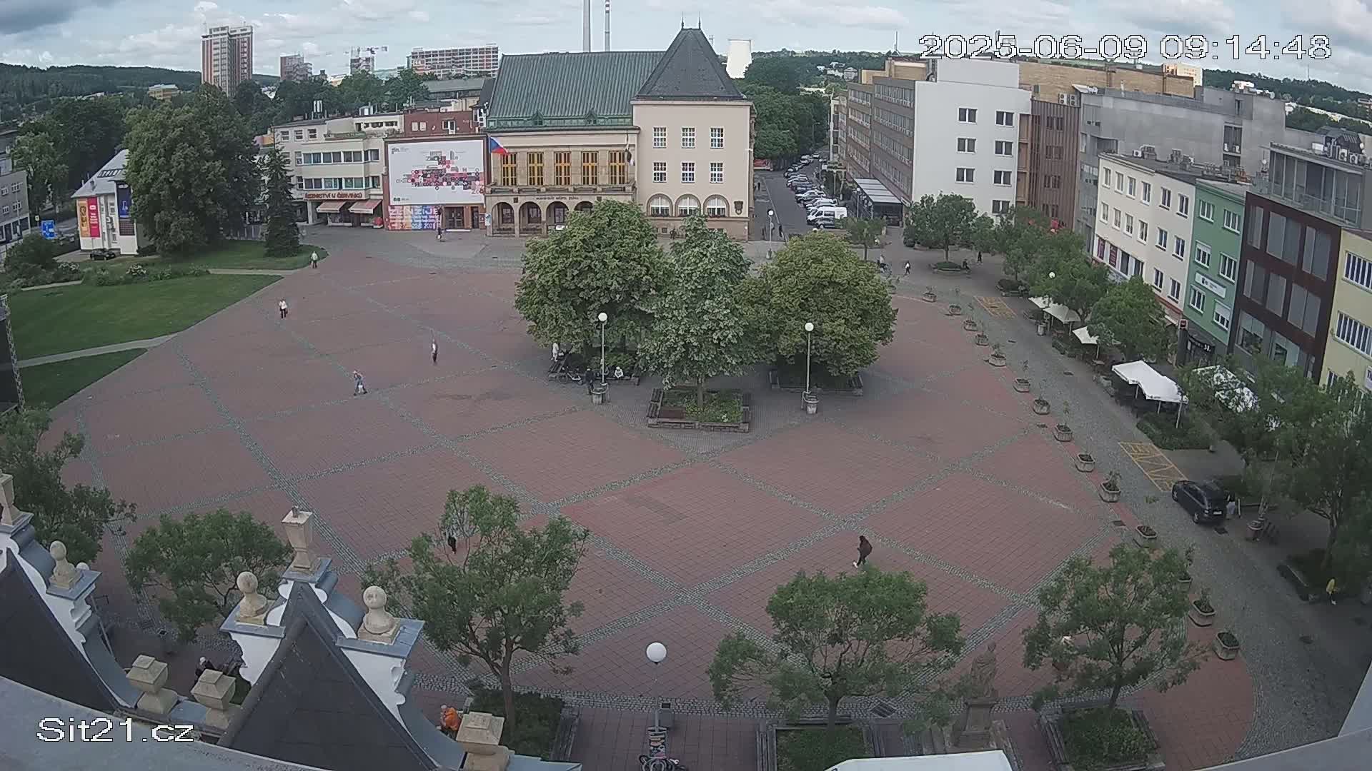 A brick town square with several trees and buildings surrounding it under a partly cloudy sky.